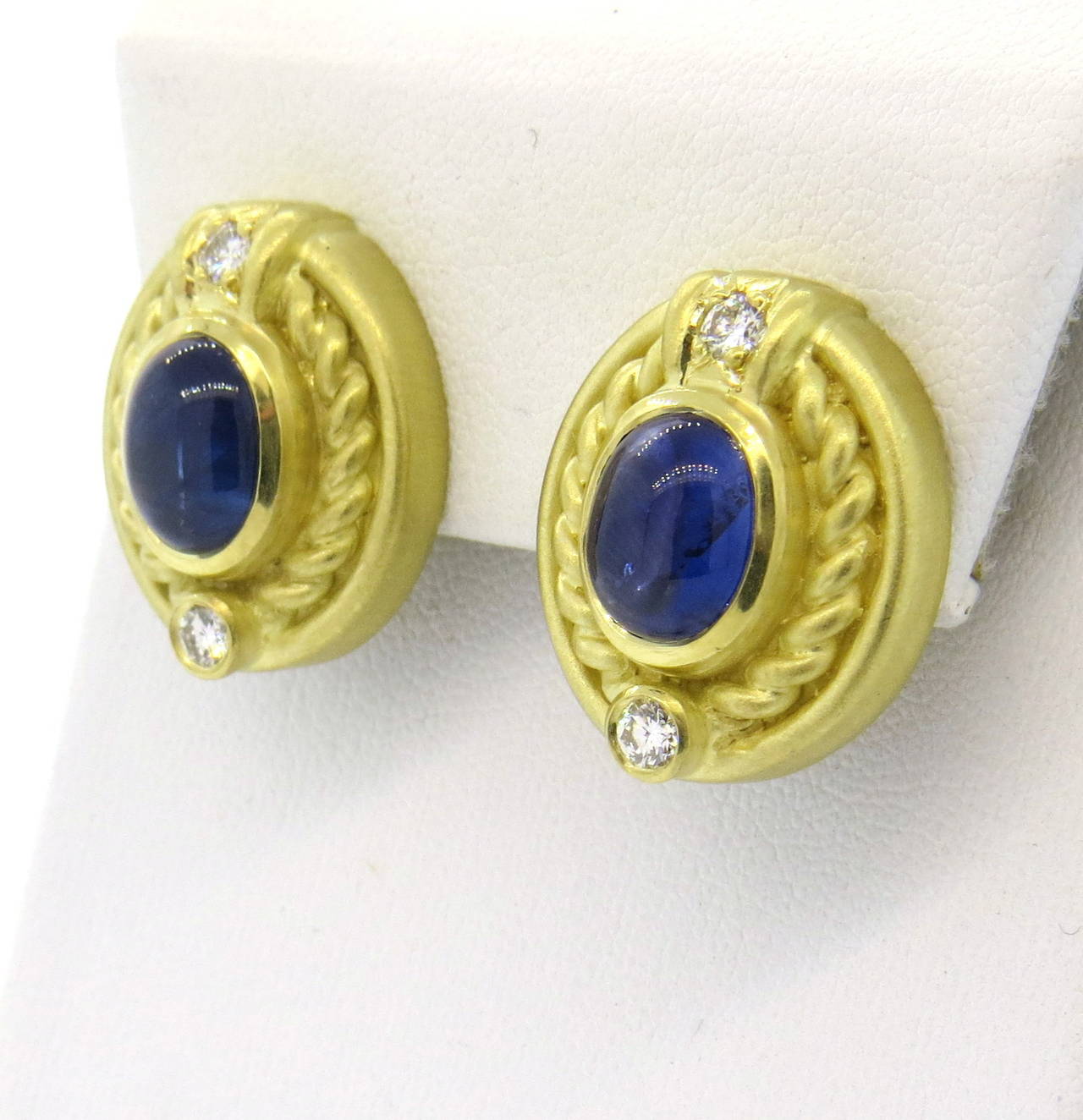 A pair of 18k yellow gold earrings set with approximately 0.48ctw in G/VS diamonds and two sapphire cabochons weighing approximately 3.60-3.80 carats .  Crafted by Judith Ripka, the earrings measure 20mm x 18mm and weigh 22.2 grams.  Drops can be