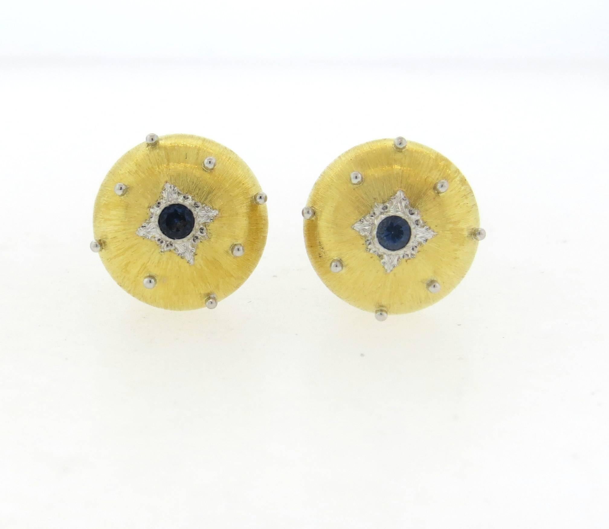 A pair of 18k yellow and white gold button earrings, crafted by Buccellati, set with blue sapphires in the center. Earrings are 16mm in diameter . Marked: Buccellati, Italy 18k G5500. Weight - 12.9 grams 