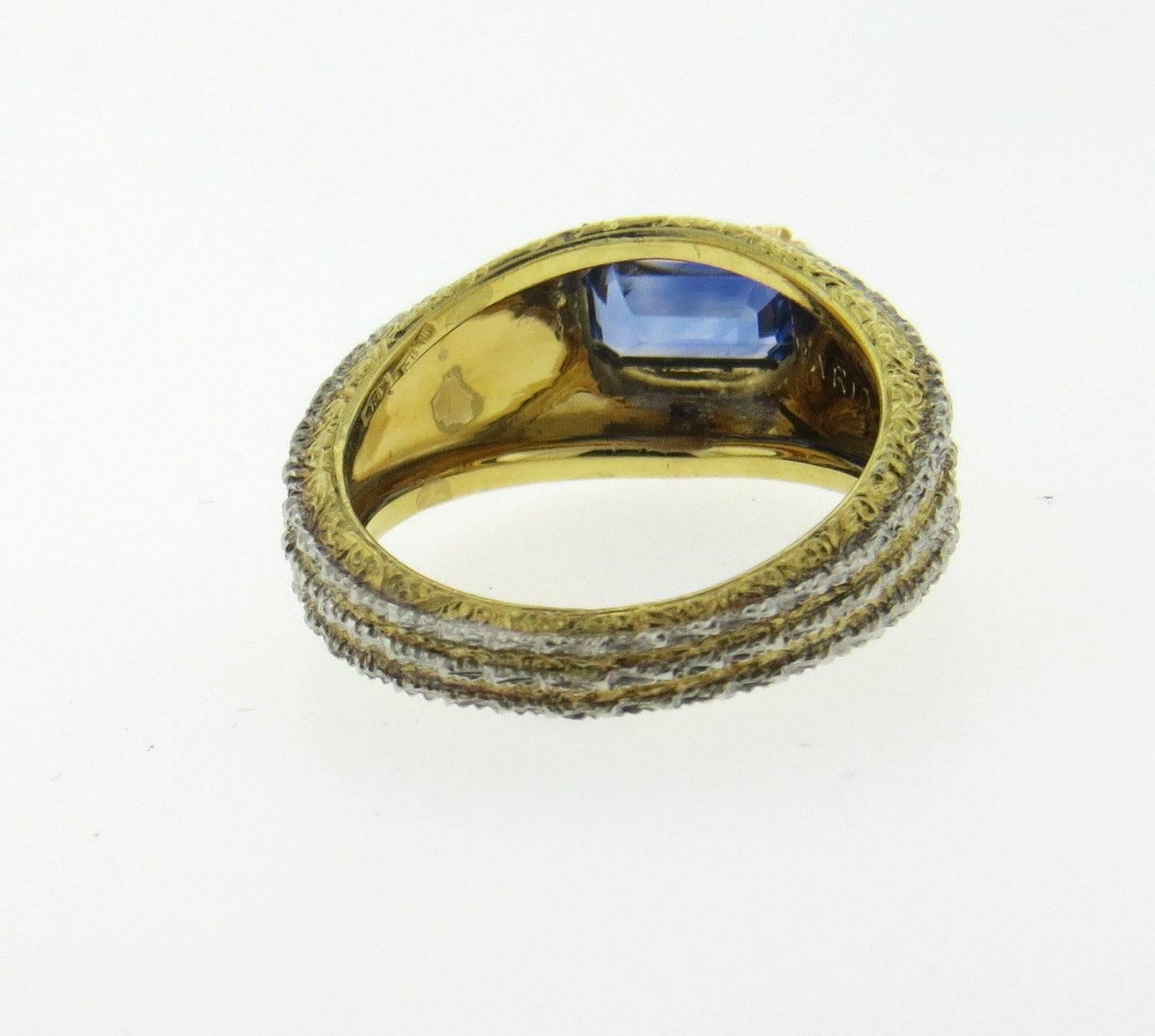 An 18k yellow and white gold ring set with a sapphire measuring 6.4mm x 4mm.  Crafted by Mario Buccellati, the ring is a size 5 1/2 and is 9.5mm at widest point  .  Marked: Mario Buccellati, 750.  The weight of the ring is 5.9 grams.  Comes with