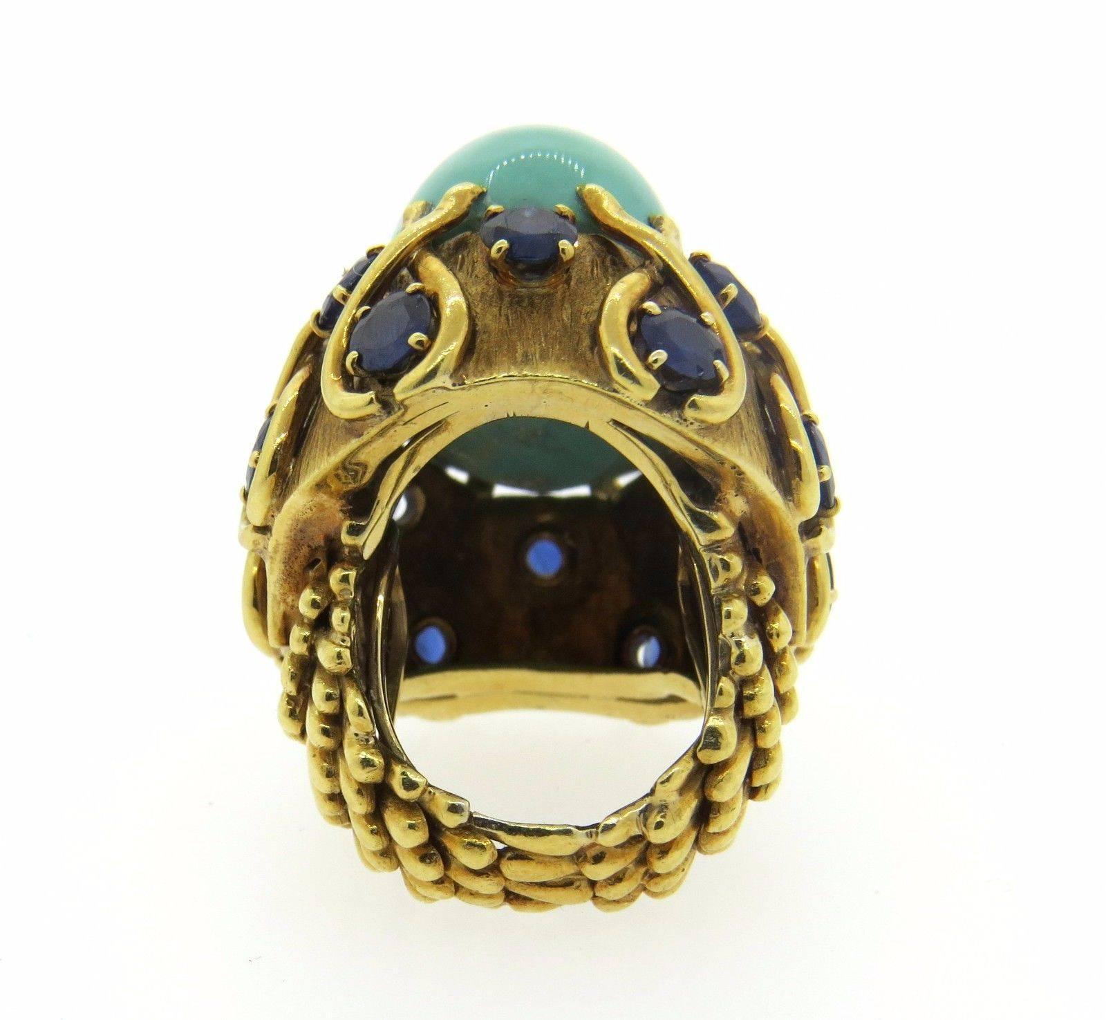 An 18k yellow gold ring set with a turquoise (26mm x 15mm x 12mm) and approximately 5.20ctw in blue sapphires.  Crafted by David Webb, the ring is a size 5, ring top measures 34mm x 27mm. Sits approx. 22mm from finger.  The weight of the piece is