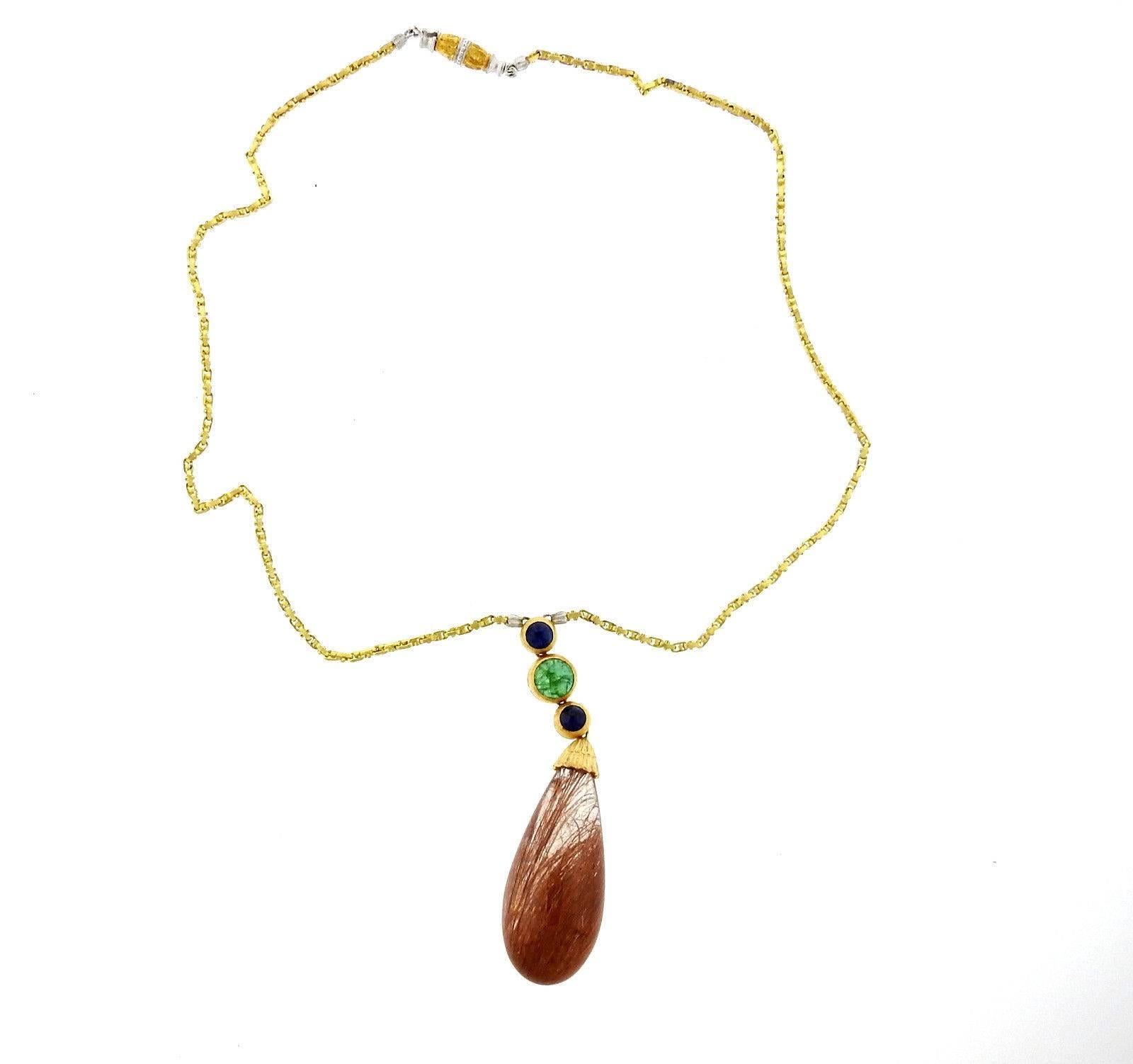 An 18k yellow and white gold necklace with a pendant featuring emerald, and sapphire cabochons accenting a large teardrop rutilated quartz (36mm x 17mm).  The necklace is 16 2/8
