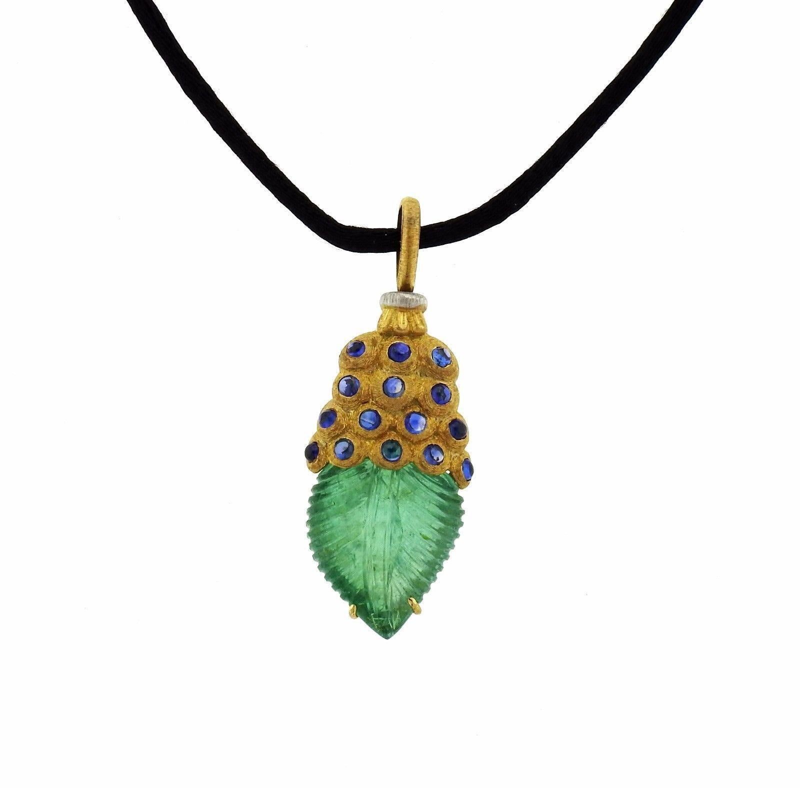 An 18k gold pendant set with blue sapphires and a carved emerald, suspended on a cord.  The pendant measures  50mm (including bale) x 20mm at widest point. The necklace length is 17.5.  The total weight of the piece is 12.3 grams.  Marked: M.