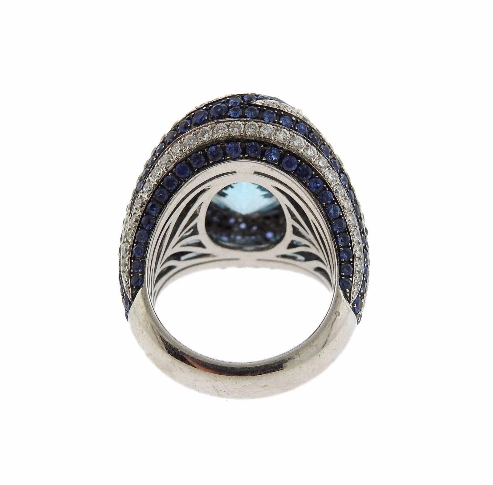 An 18k white gold ring set with a blue topaz (18mm x 13mm) 1.53ctw of G/VS diamonds and sapphires. The ring is a size 7. The ring top is 23mm wide.  The weight of the ring is 23.2 grams.  Marked: Asprey, 750