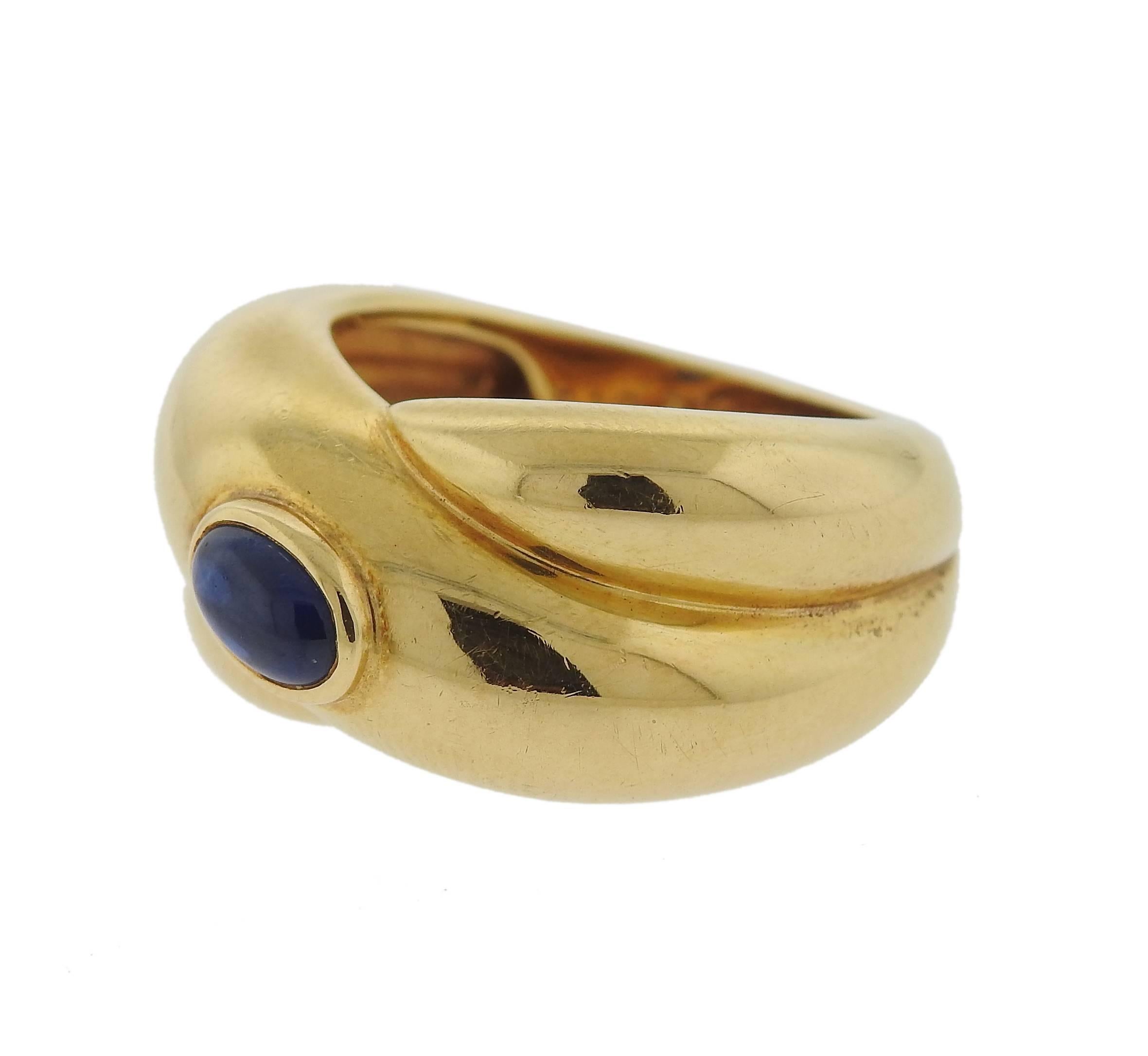 18k yellow gold crossover ring, crafted by Cartier, set with an oval sapphire cabochon in the center. Ring is a size 5 and is 11mm wide. Marked:  49,  Cartier, 1992, 750, C12572. Weight of the piece - 8.8 grams