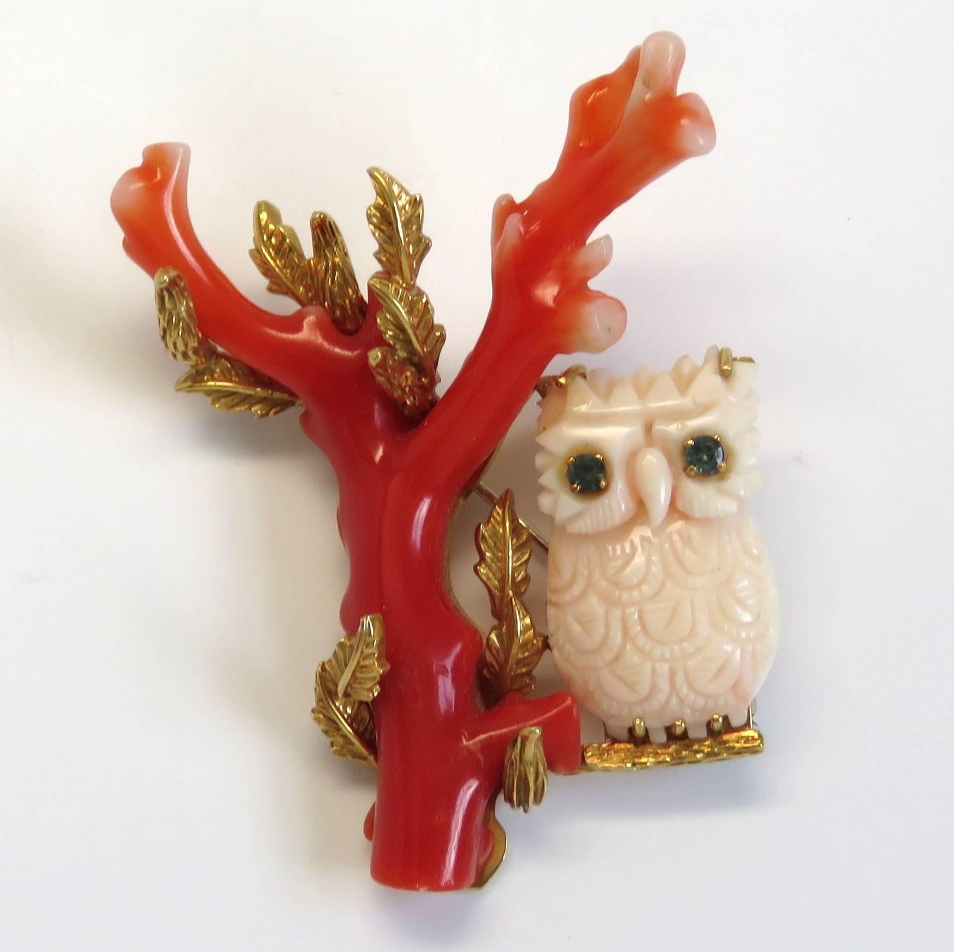 A 14k gold brooch adorned with red and angel skin coral, which depicts an owl with sapphire eyes sitting on a branch.  The piece measures 60mm x 44mm and weighs 22 grams.