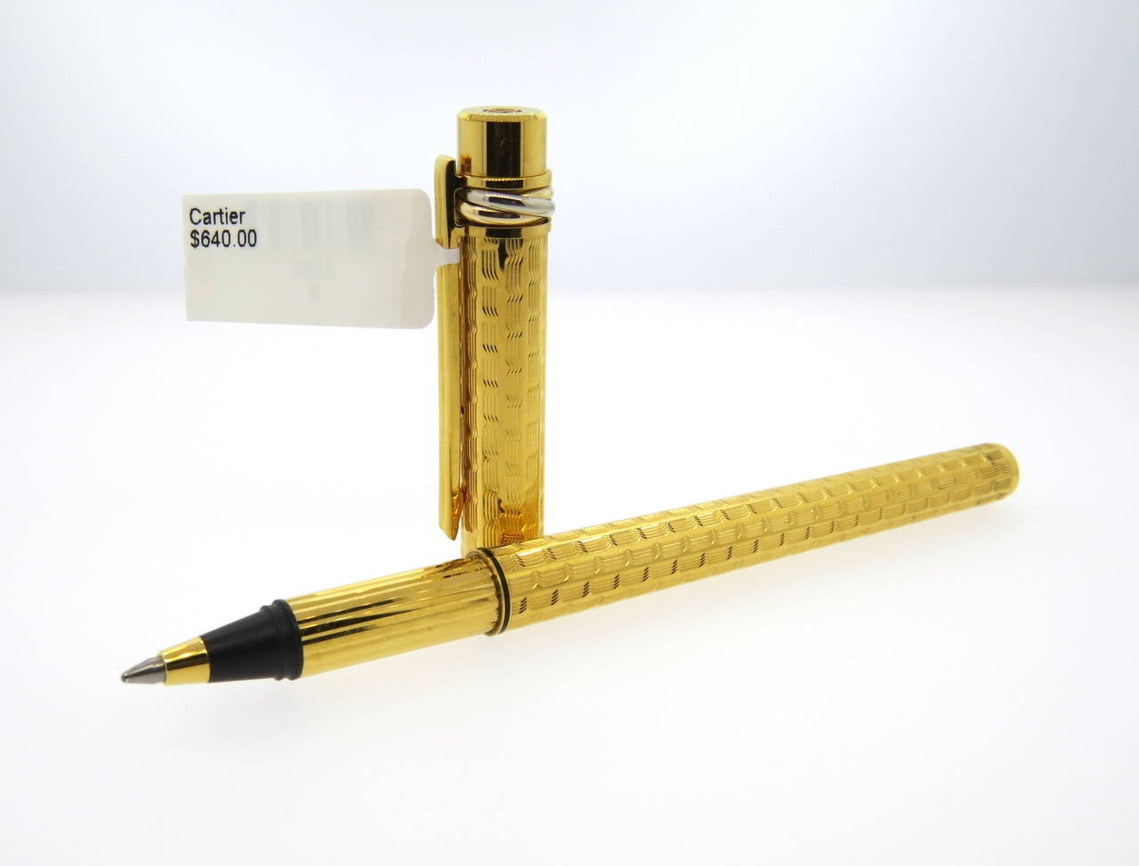 Bold Cartier Must de Cartier ballpoint pen featuring a gold textured finish and classic three trinity rings on the pen cap. Pen measures 138mm long. Pen is a brand new in store sample, comes with original box, papers and cartridges. Pen retails for