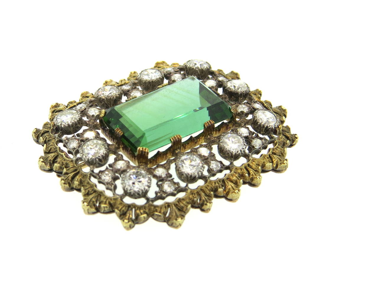 Impressive 18k gold brooch, crafted by Buccellati, featuring approximately 13ct emerald cut green tourmaline as a centerpiece, surrounded with approx. 3.00ctw in GH/VS diamonds. Brooch measures 41mm x 35mm. Marked Buccellati and 750. Weight of the