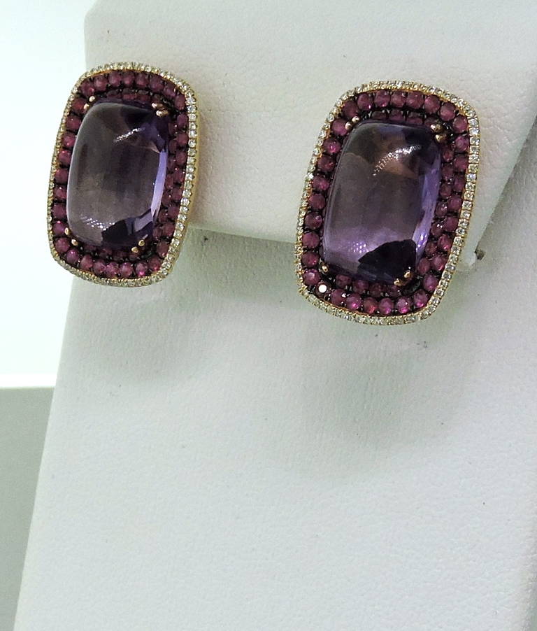 Lovely pair of 18K rose gold earrings featuring amethyst cabochons surrounded by pave rubies and diamonds. Amethyst cabochons total approx. 17.85ctw, Rubies approx. 2.24ctw and approx. 0.54ctw of diamonds. Earrings measure 22.5mm x 17mm. Marked