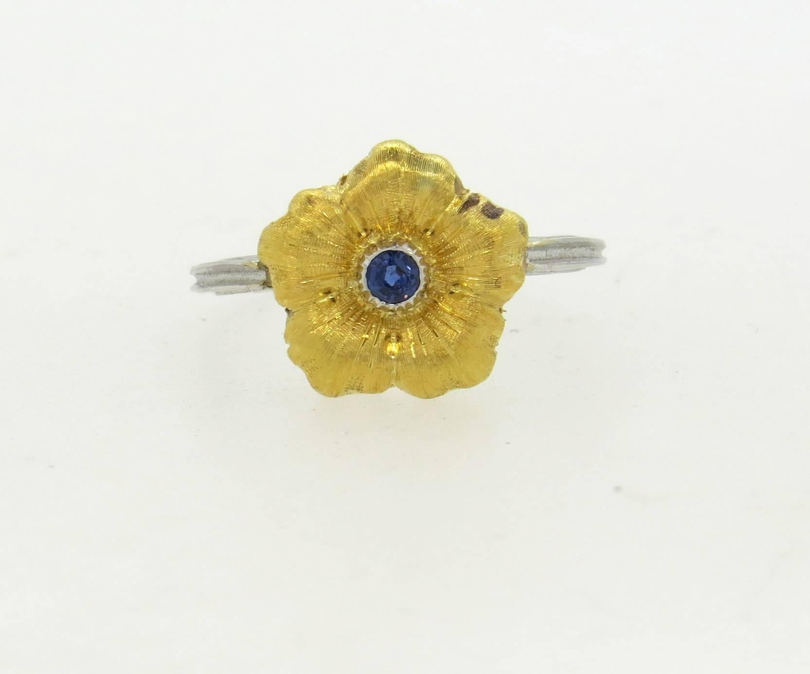 18k white and yellow gold ring, crafted by Buccellati, featuring flower top, decorated with a 0.12ct blue sapphire in the center. Ring is a size 7, ring top is 12mm x 14mm. Marked: Italy 18k, Buccellati. Weight of the piece - 3.2 grams
Comes with