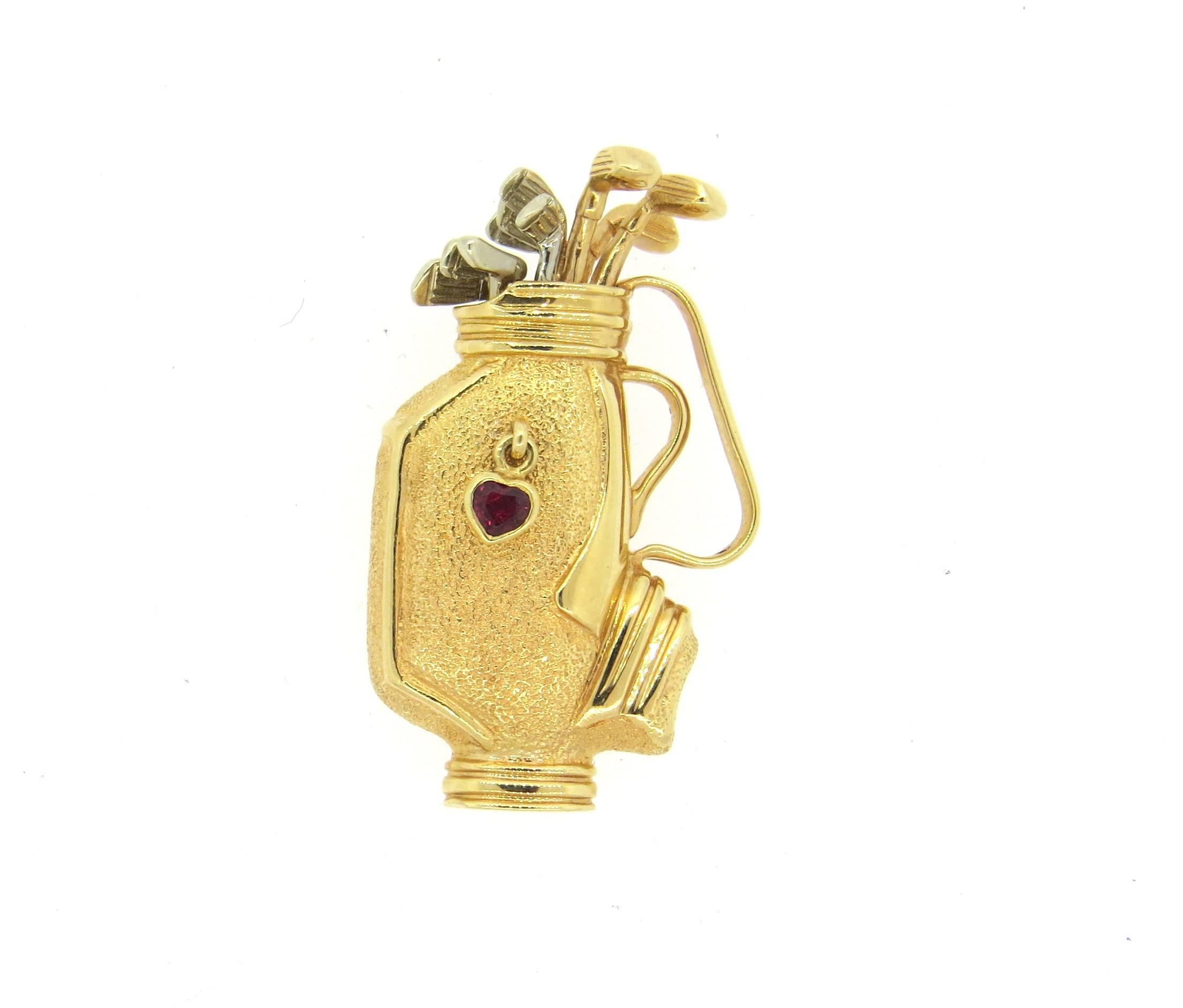 14k yellow and white gold brooch, depicting a golf bag, decorated with garnet heart charm. Brooch measures 38mm x 22mm. Weight of the piece - 11.6 grams