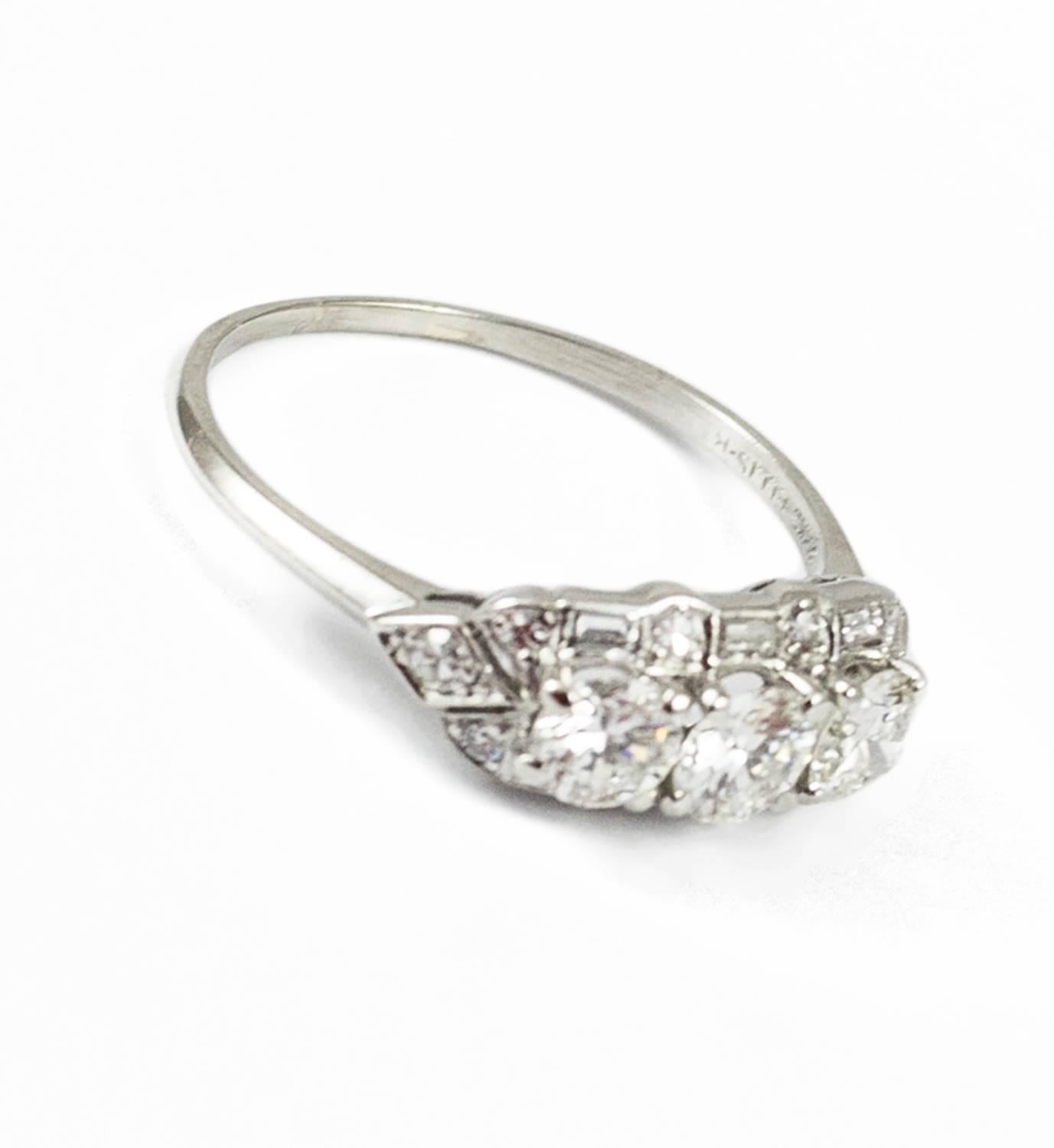 This lovely ring was made circa 1935. It is set in platinum and holds three bright central round brilliant cut diamonds. (.34 ct, I-J VS1 plus 2 = .53 J-K VS2-SI1). Additionally the central diamonds are framed by  6 baguette cut and 10 round single