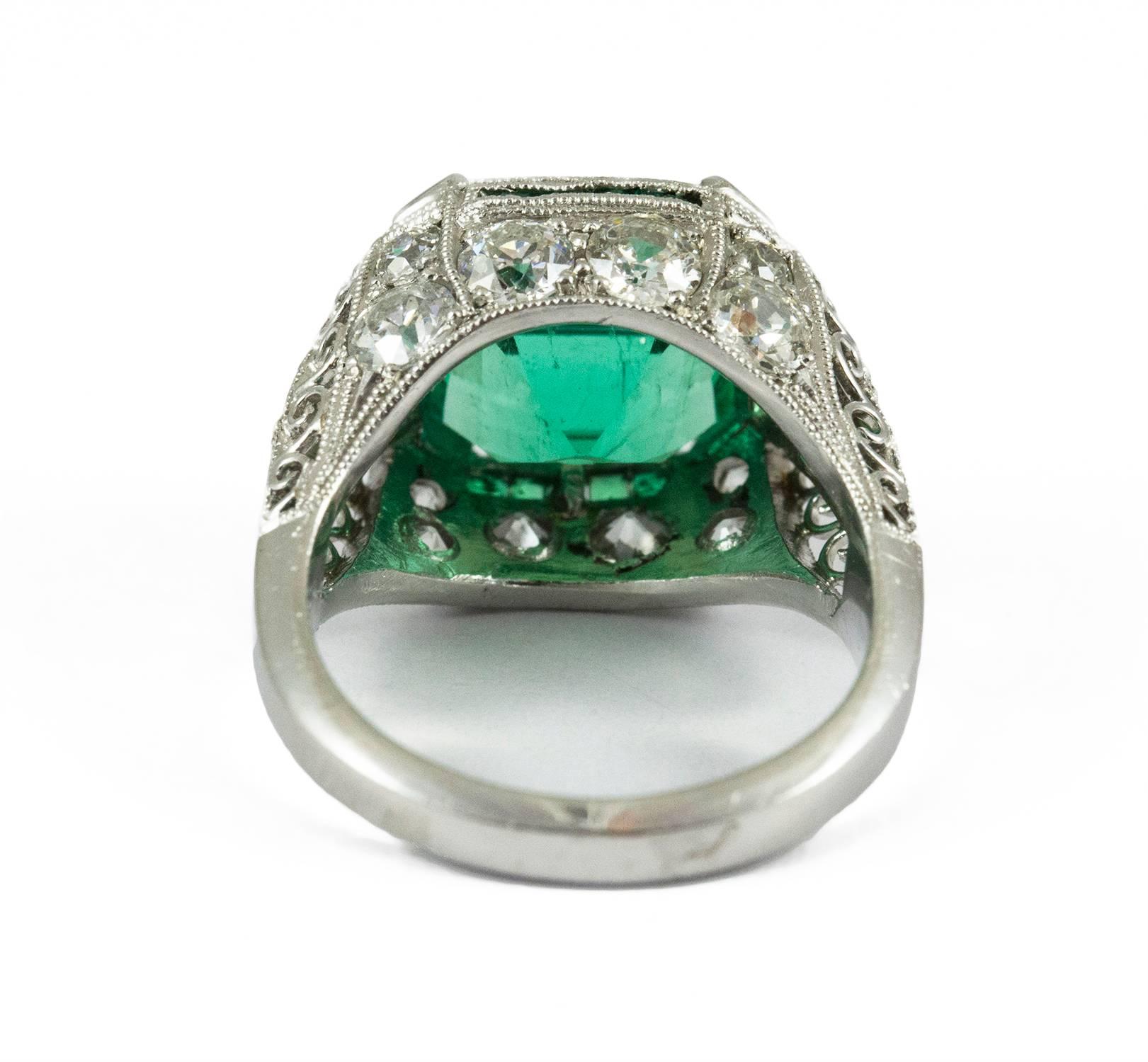 This ravishing Art Deco Emerald ring is set in platinum with a bright 6.48 rectangular mixed cut emerald. The central stone is embellished by eighteen old European cut bead set diamonds. (F-G-H, VS2-I1) Additionally there are twenty one delicate