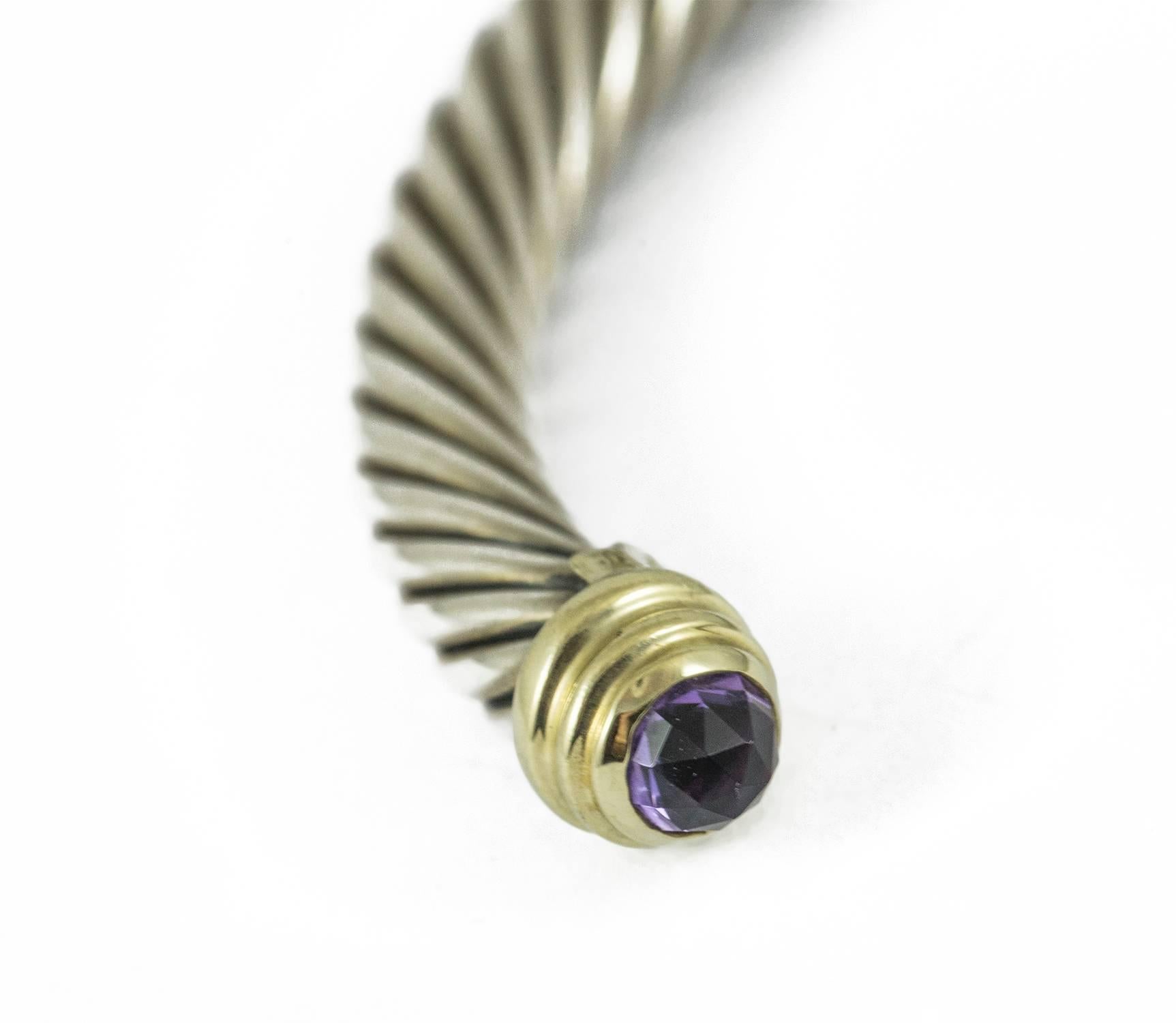A David Yurman Silver, 14k yellow gold and amethyst bangle. The gemstones are set in yellow gold which tips the bangle opening. This bracelet is in excellent condition and is medium in size.