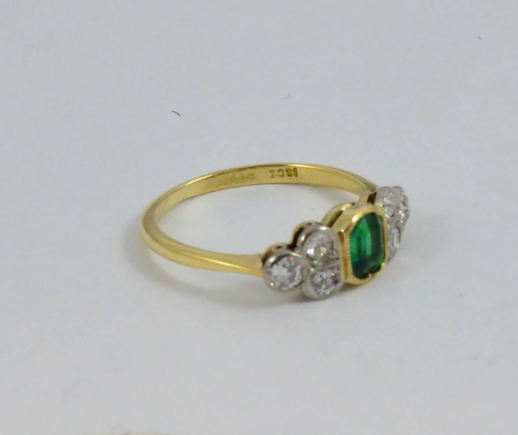 A charming bright vintage ring holding an intense rich green .60 ct. rectangular step cut emerald embellished by six old European cut diamonds (.44ct). The ring is custom made in platinum and 18kt yellow gold with detailed mill grain workmanship. It
