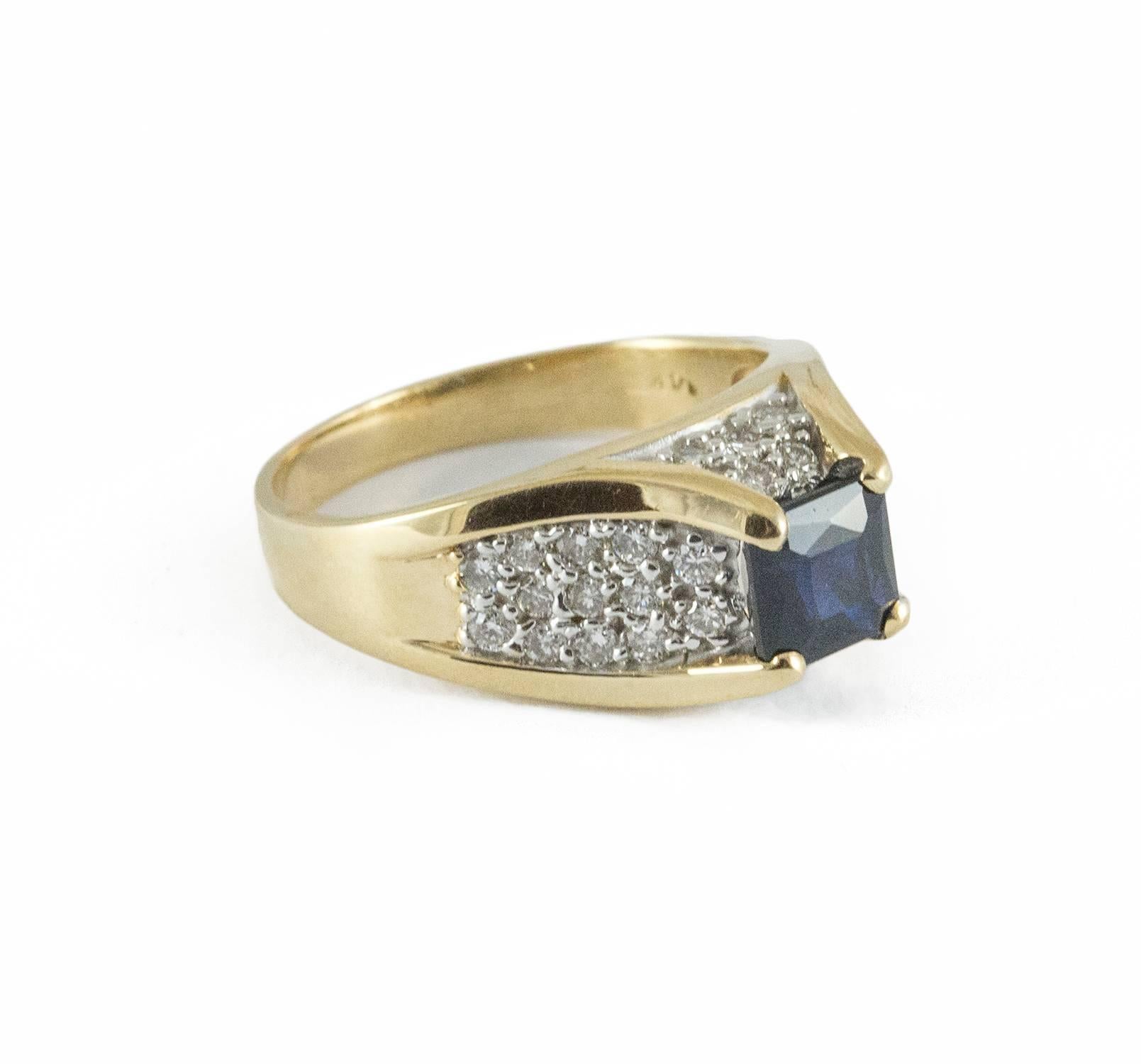 A bold vintage ring with a central square cut dark toned sapphire weighing 1.5 ct. Enhancing the central stone are 36 round brilliant cut diamonds weighing .62 ct. (SI-I1,G-H). The mount is 14kt yellow gold and the sapphire sits dramatically above