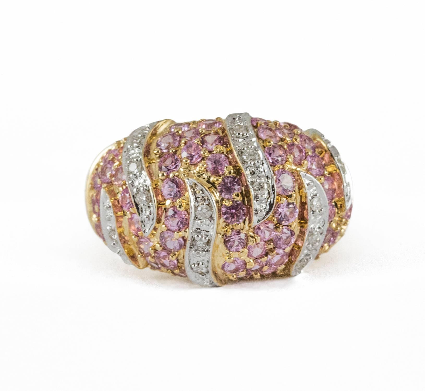 A 14kt yellow and white gold contemporary dome ring set with 61 pink sapphires and 14 round brilliant cut diamonds. The sapphires and diamonds are bead set with the sapphires totaling 3.90 ct. and the diamonds totalling .17 ct. This ring is dramatic