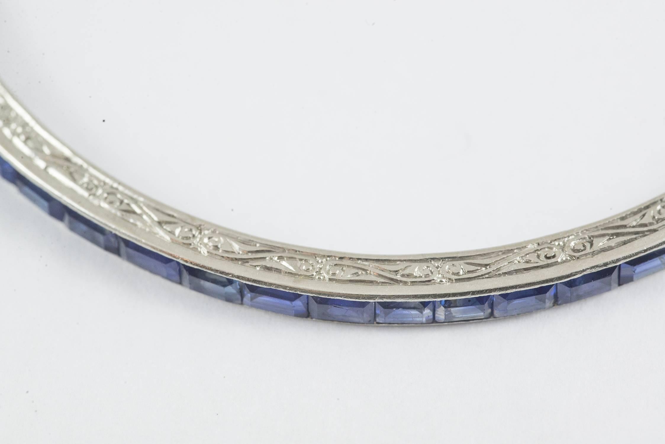 A rare Art Deco bangle set in platinum with 55 rectangular step cut blue sapphires. This bangle is beautifully made with fine hand engraved scrolls carved into the platinum frame. The diameter is 2.5 inches and the interior circumference is 7.5
