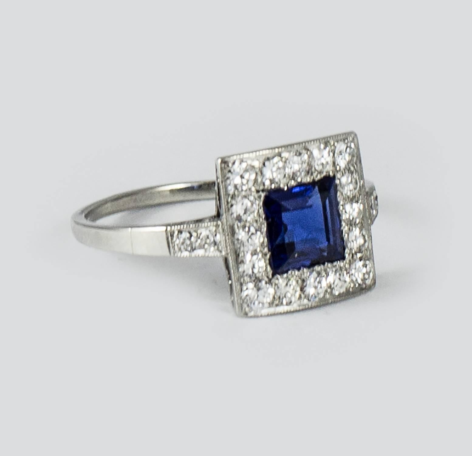 A delightful Art Deco Sapphire ring set in platinum. The custom made mount holds a deep blue step cut square sapphire weighing .90 ct. It is framed by 20 excellent quality bead set old European cut diamonds. The ring has lovely hand mill grain