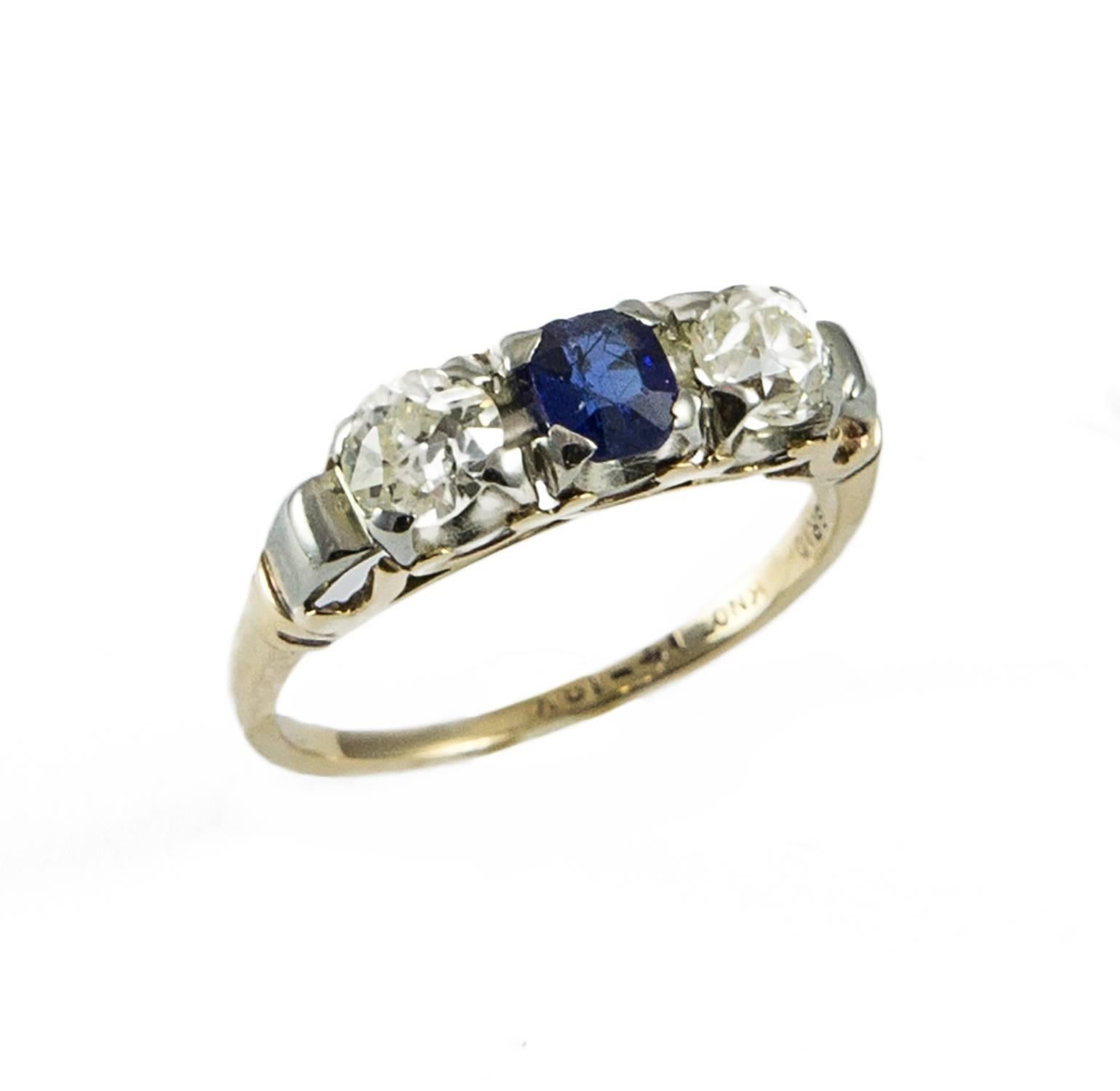 A vintage three stone diamond and sapphire ring set in 18k yellow and white gold. The two old European cut diamonds total (.59 tw. SI-I1, J-K). The bright blue sapphire weighs .40 ct. The mount is custom made with hand finishing and this ring would