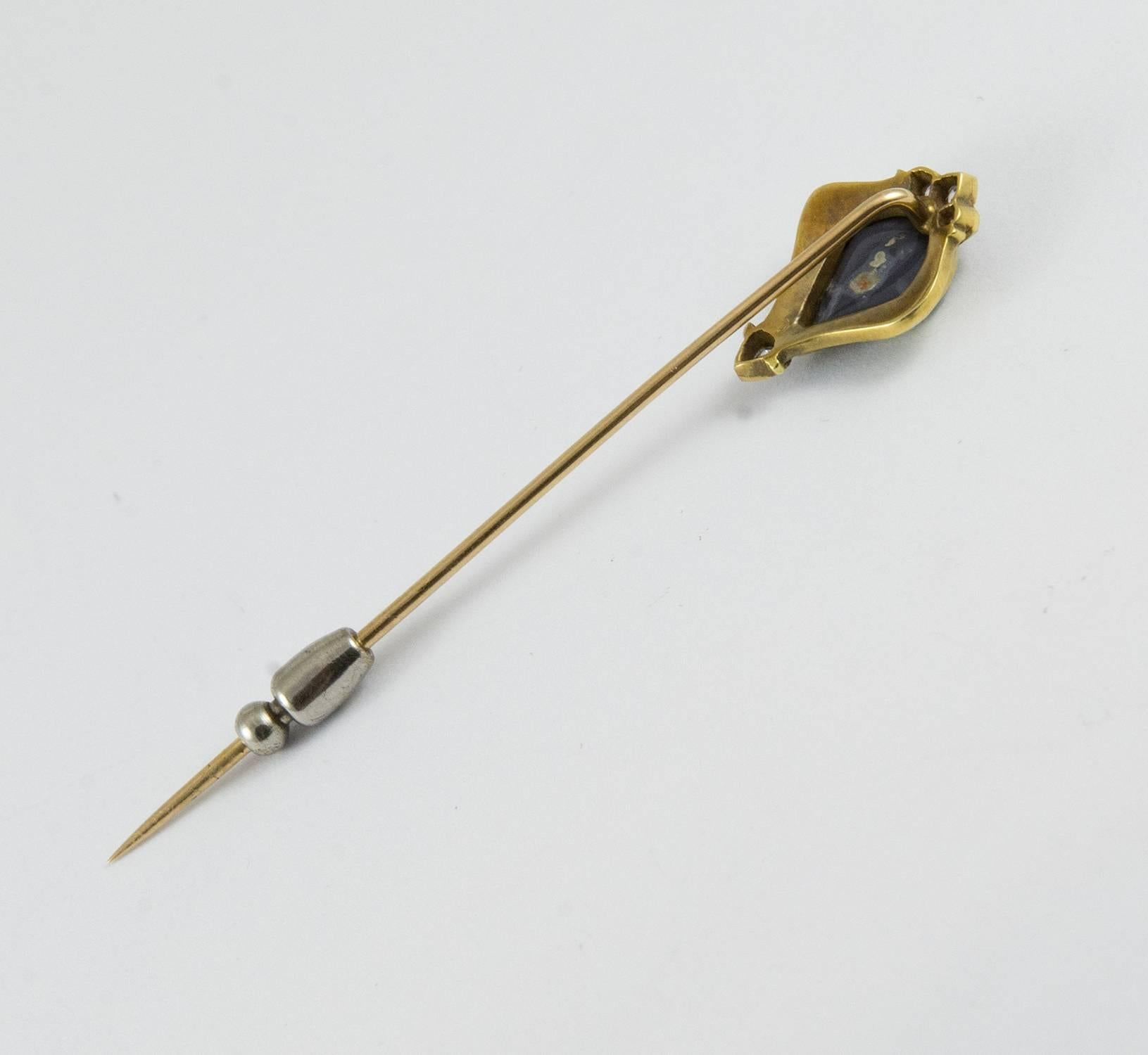 A stunning Art Nouveau stick pin made Circa 1915. It holds a beautiful 1.65 ct. cabochon black opal with strong play of colour. There are four old European cut diamonds which are bead set above and below the central gem.The entire opal is framed in