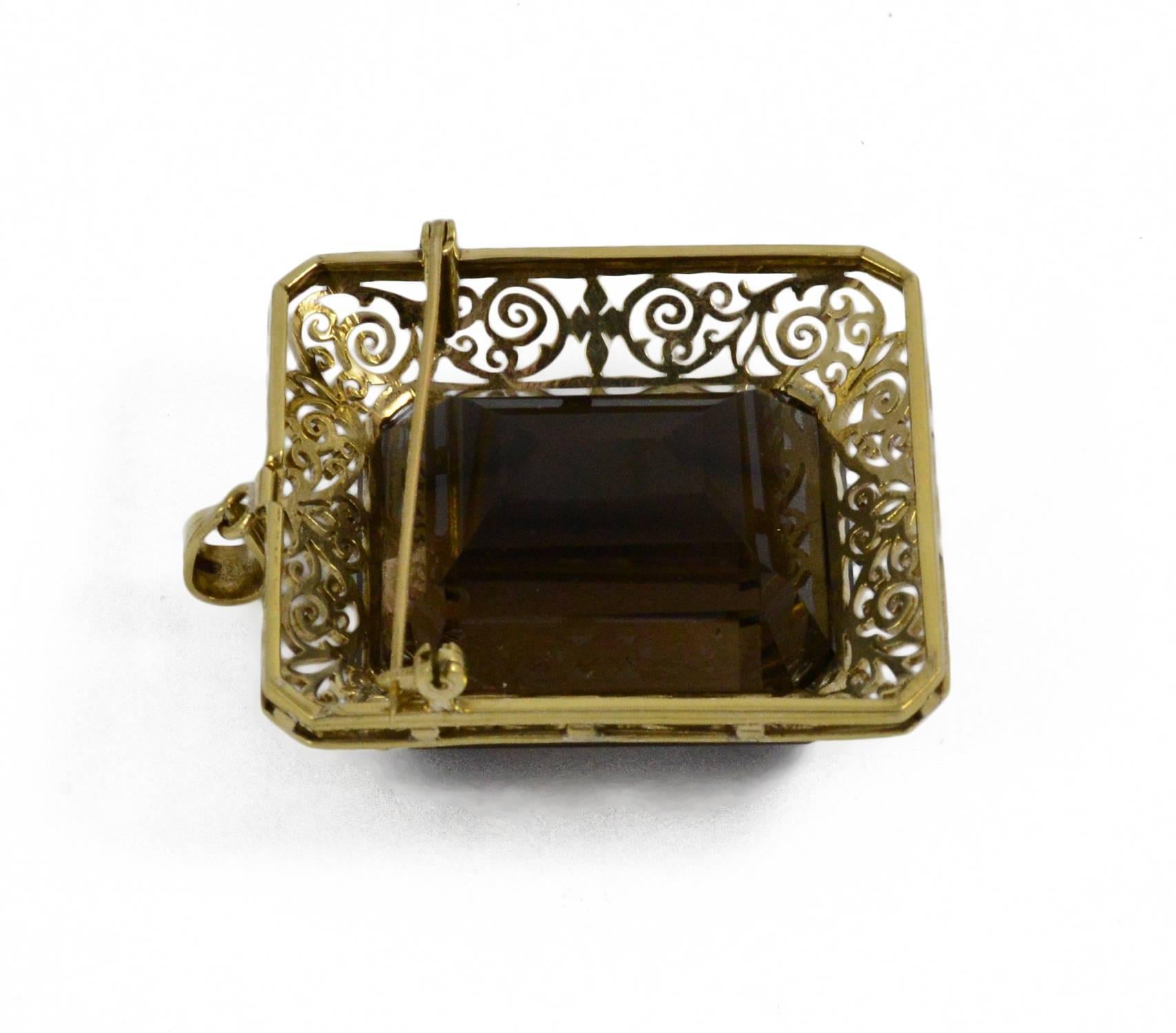 A large bold rectangular step cut smokey quartz set in a intricate custom made 14kt yellow gold frame. This pendant also can be worn as a brooch and comes with a 18 inch gold chain. It is in excellent condition.