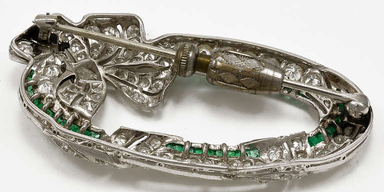 A striking Art Deco Emerald and Diamond Platinum Oval Ribbon Brooch. 

This Art Deco Brooch has 105 Old mine cut Diamonds of  H-I color VS/SI with a total weight of 5.75cts with 44 caliber-cut Emeralds approximately 1.10 cts. total weight.