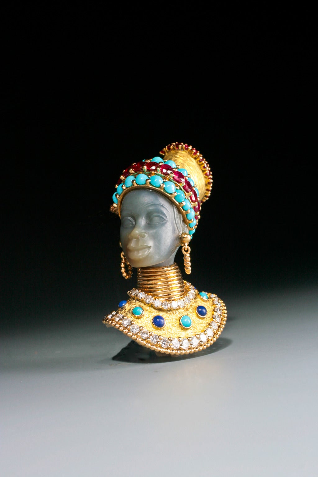 An unusual agate, diamond and multi gem traditional Kenya Nandi Tribe Princess  head brooch, the carved agate head topped with a turquoise and ruby turban, adorned with gold earrings and collar, the sculpted gold breastplate set with lapis,