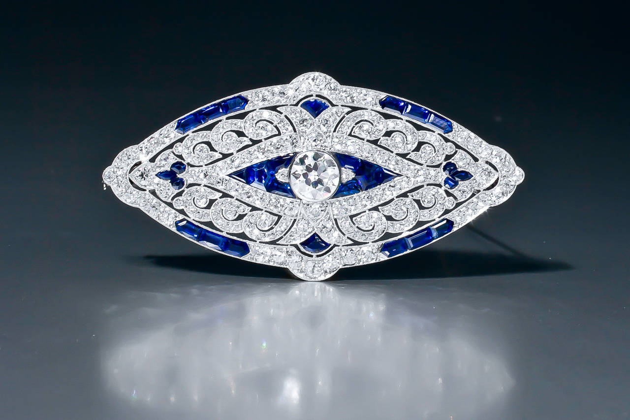 An Art Deco sapphire and diamond brooch by Mauboussin, Paris, set throughout with old European cut and single cut diamonds and calibré-cut sapphires. The open work platinum mount shows the typical 'mille grains' finish.

Accompanied by the