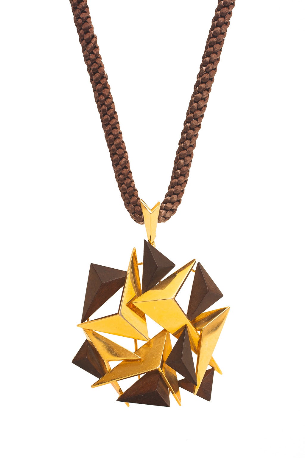 A gold & wood Modernist pendant-brooch on a silk cord by Fred Paris, composed of a cluster of various sizes of triangular forms of 18 karat yellow gold and wood, accompanied by finely braided dark brown silk cord. The pendant is fitted with a bail