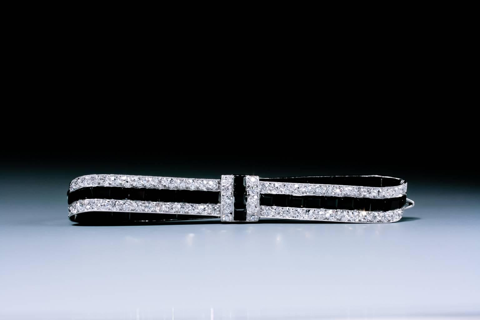 A very fine early Art Deco onyx and diamond bow brooch by Cartier, the horizontally aligned ribbon bow set with a central row of square cut onyx between courses of circular cut diamonds, backed on both sides with graduated calibré-cut onyx, mounted