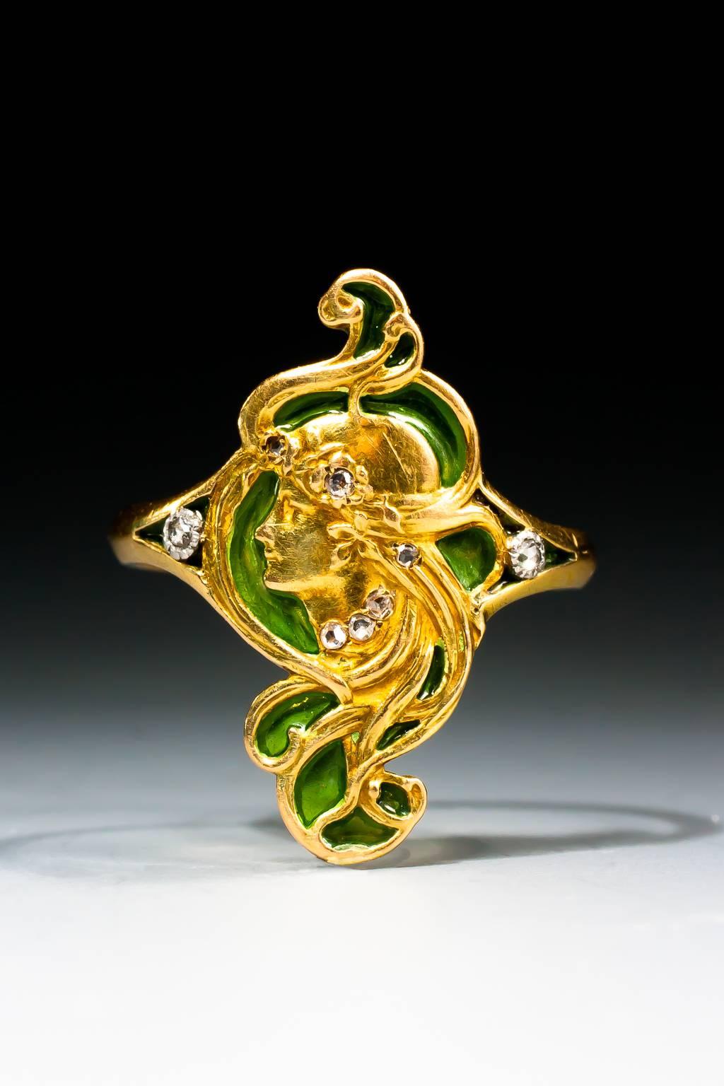 A very fine Art Nouveau gold, diamond and plique-à-jour enamel ring by André Rambour, depicting the face of a maiden in profile, with undulating tresses and rose cut diamond highlights, wearing a rose cut diamond necklace, on a green