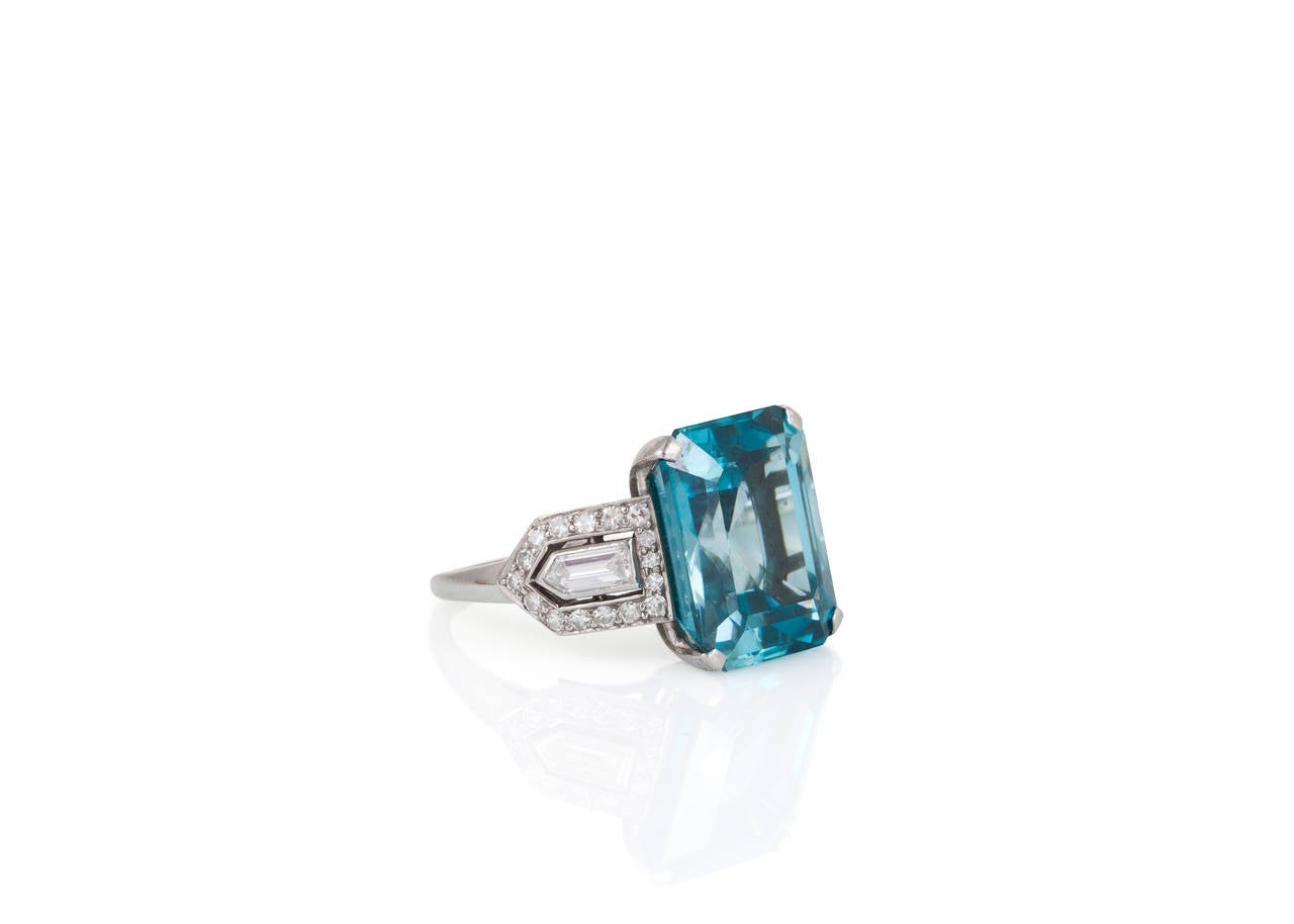 Featuring a beautiful emerald cut blue zircon weighing an estimated 10 carats, this ring also incorporates two bullet shaped diamonds, circled by a diamond trim in an Art Deco style.
Ring Size: 6 ½