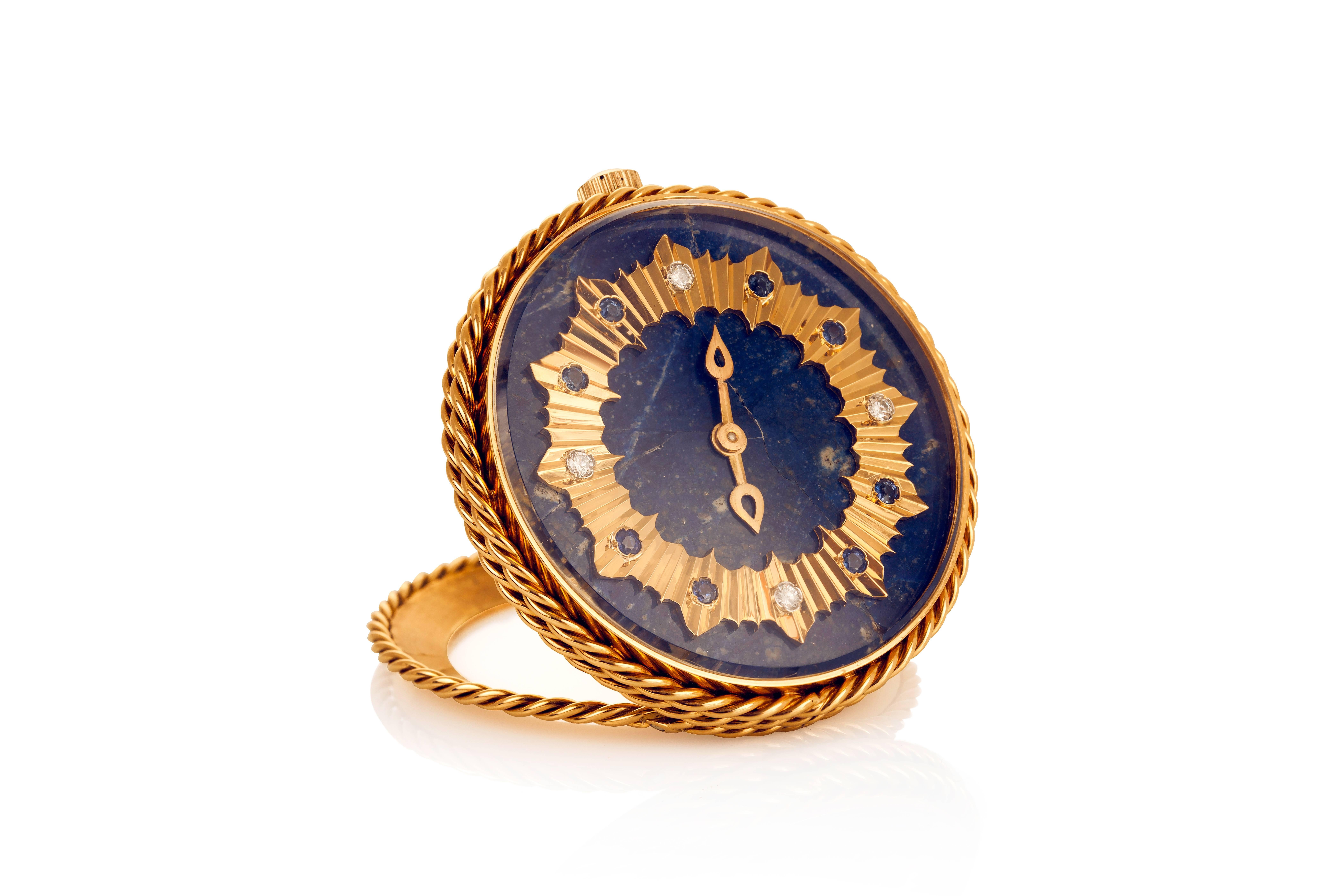 This beautifully detailed travel clock features a lapis lazuli face with a yellow gold sunburst with sapphire and diamond hour markers and a gold braided rope surrounding the case and fold-down stand.