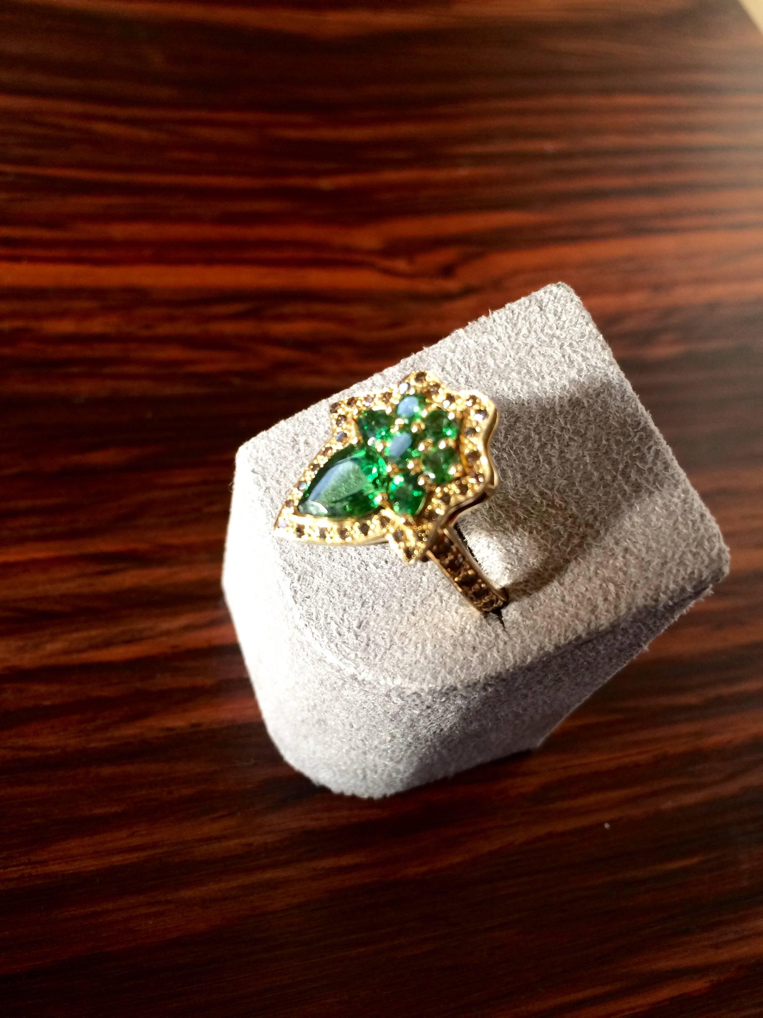 This ring has been handcrafted in London from 18ct yellow gold and is set with vivid green tsavorites which total 1.82ct and natural cognac diamonds, totalling 0.15ct. 

Diameter: 1.7cm
Length: 2.1cm

It is a ring size N 1/2 Uk or 6 3/4 US and can