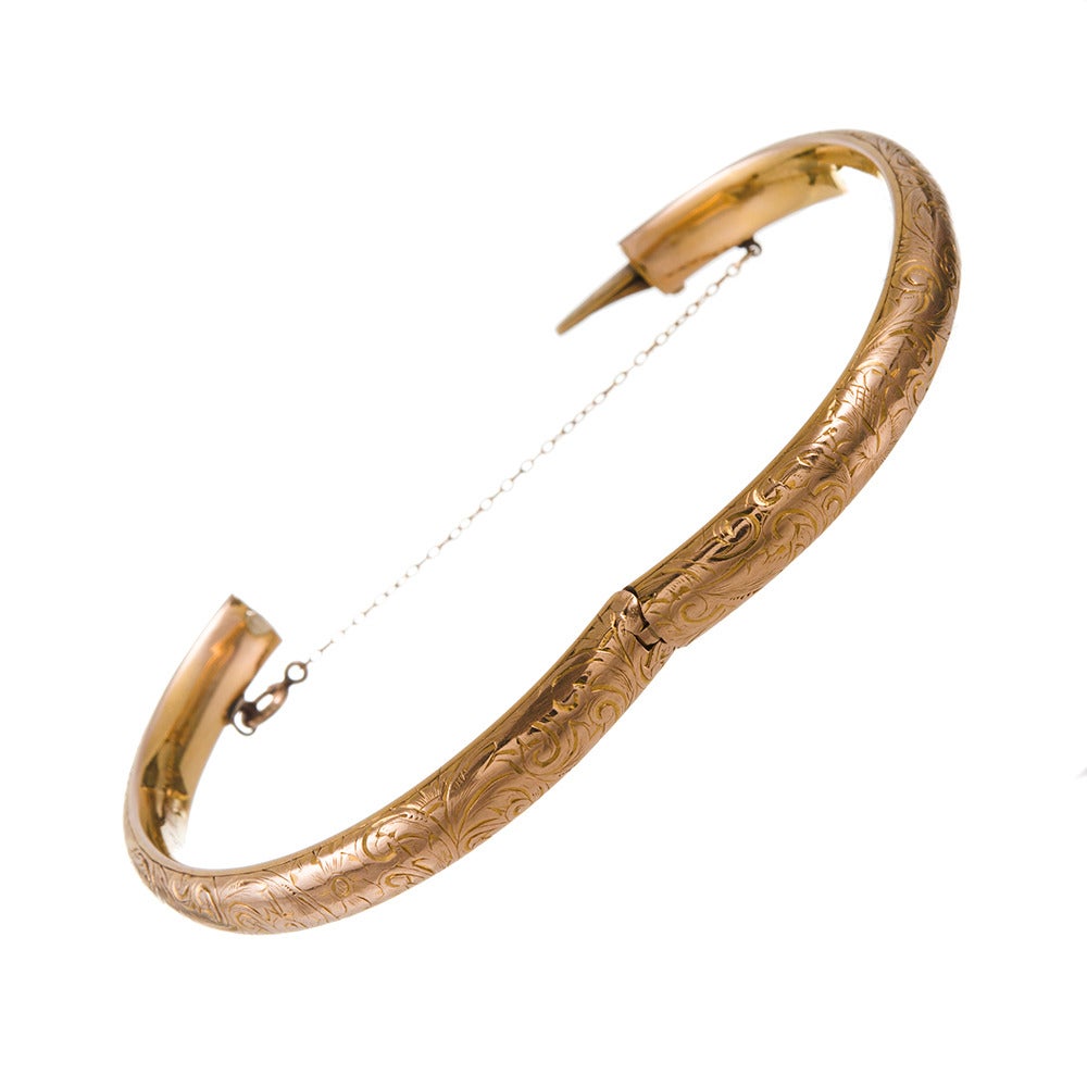 14k yellow gold bangle, made in America. A gentle oval shape keeps the bracelet in place and comfortable on the wrist. It is heavily decorated with a hand-engraved filigree pattern, opens with a single hinge and is finished with a safety chain. 2