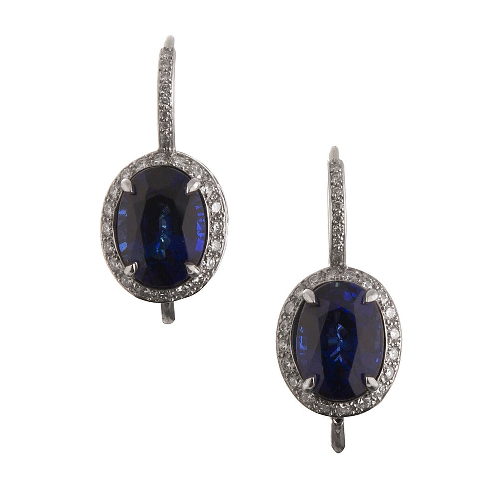 A modern pair of earrings that will certainly become a classic heirloom, these drop earrings are rendered in platinum and measure 7/8 of an inch in overall length. The center sapphires are exquisitely royal blue, faceted ovals that weigh 6.73 carats