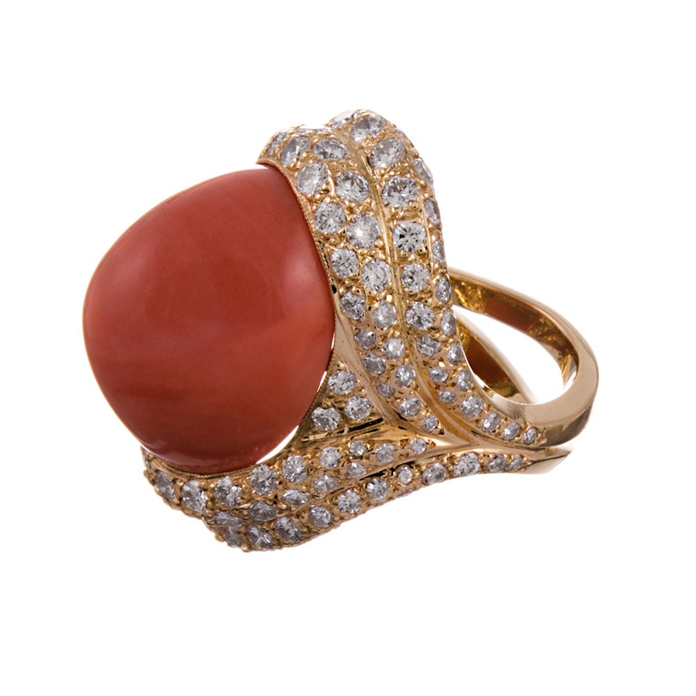 Evoking much of the sophisticated structure classically attributed to Van Clef & Arpels, this is a striking piece to enhance nearly any attire. Sweeping strokes of gold, dotted with diamonds provide the ideal frame for a large coral cabochon. Made