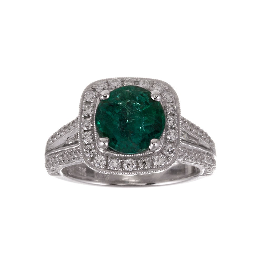 A hint of unexpected, with a 2.21 round emerald set in an 18k white gold diamond mounting and finished with mille grain edges. There are tapered baguette diamonds sloping down the shoulders between two rows of round diamonds. The round center stone,