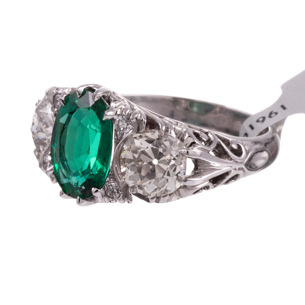 18k white gold ring, traditional English Carved style with a 2.25 carat oval emerald center and flanked by a pair of old European cut diamonds. The emerald is remarkably transparent and unincluded. It looks larger than the weight would suggest. The