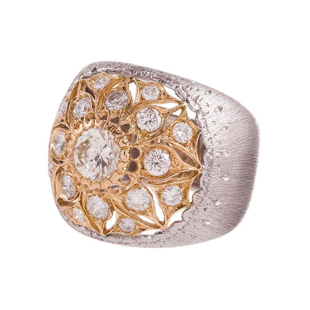 An 18 karat white gold ring designed with a low-profile dome shape and finished with Buccellati’s signature texture, resembling golden fabric. The center is a cluster of diamonds set in 18 karat yellow gold and arranged into a flower motif. The