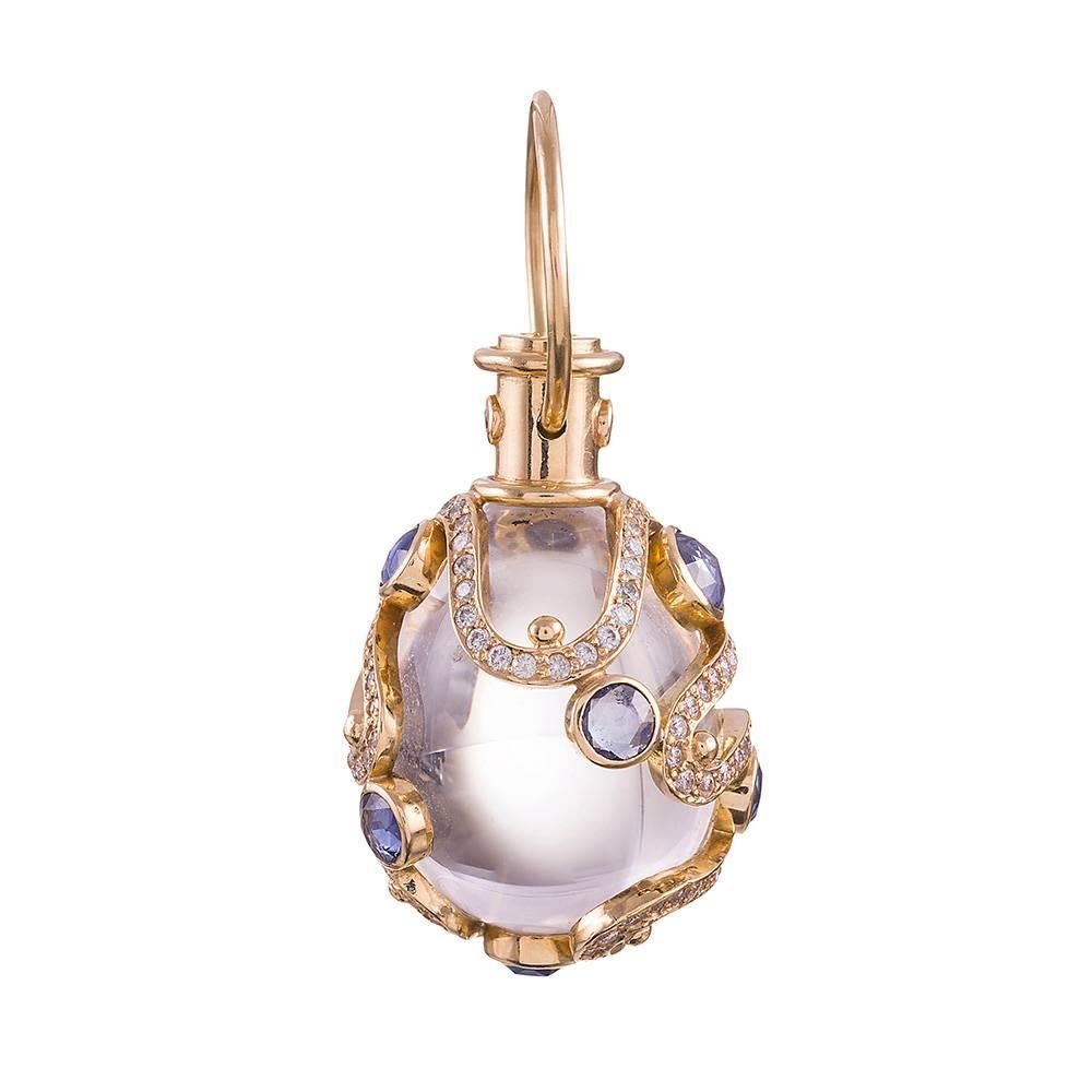 A mystical pendant appearing as if a genie might spring forth from it at any moment, this rock crystal creation is decorated with a scrolling pattern of diamonds and light blue sapphires. The gemstones weigh 1.33 and 1.35 carats in total