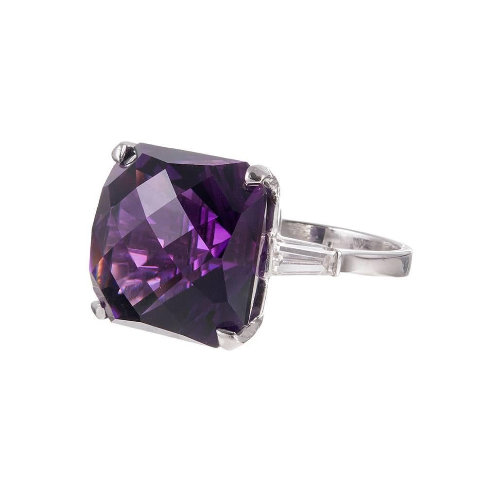 A classic platinum setting unexpectedly set with a “checkerboard” cut amethyst and flanked by a pair of baguette white diamonds. This timeless mounting style is rarely seen with such a center stone, but it adds a hint of whimsy to the simple design