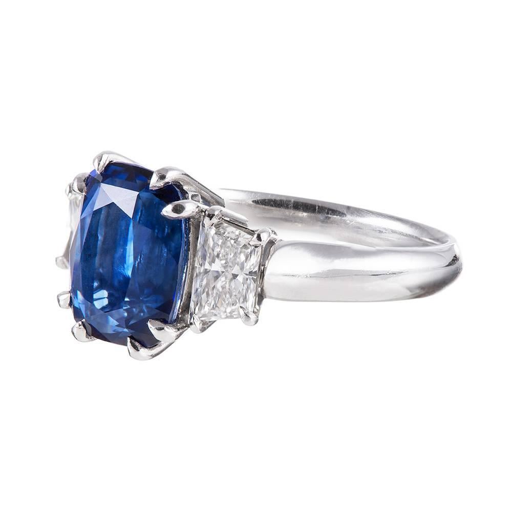 A classic creation set in the center with a 4.12 carat elongated cushion brilliant sapphire an flanked by a pair of trapezoid diamonds. The diamonds weigh .86 carat combined and are the ideal accent for the major stone, tapering down the sides and
