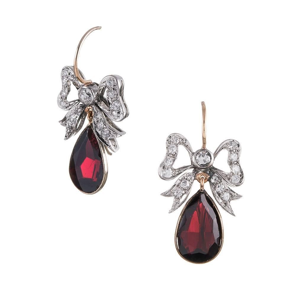 Made of platinum and 14k rose gold, these sweet earrings are designed as a diamond-studded bow from which is suspended a pear-shaped faceted garnet. At 1.25 inches long, these can be worn and enjoyed every day.