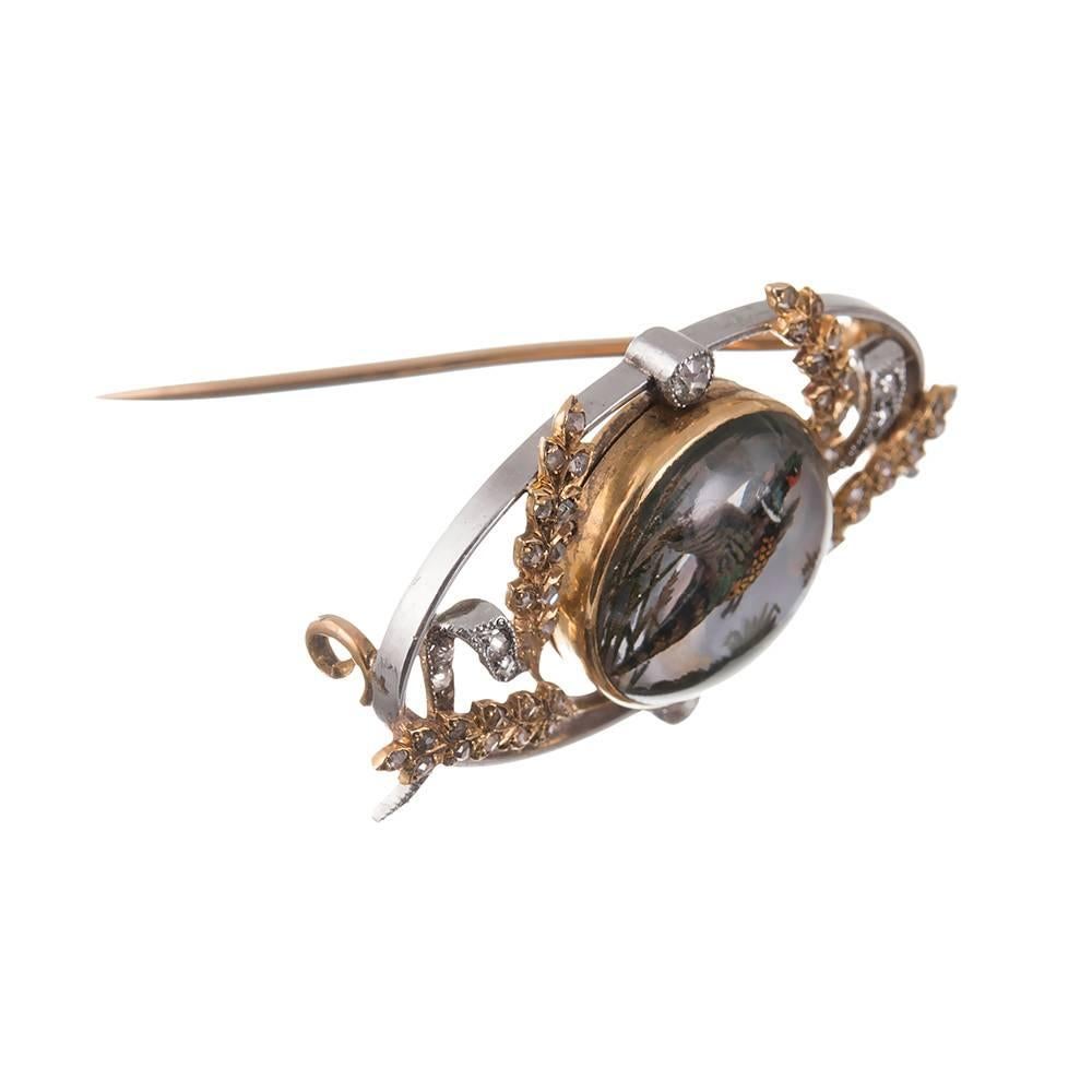 An absolutely splendid antique treasure, rendered in 18k yellow gold and platinum. The Essex crystal depicts a pheasant in flight and is surrounded by a garland of rose cut diamond studded branches and scrolling accents. 1 1/2 by 7/8 inches, offered