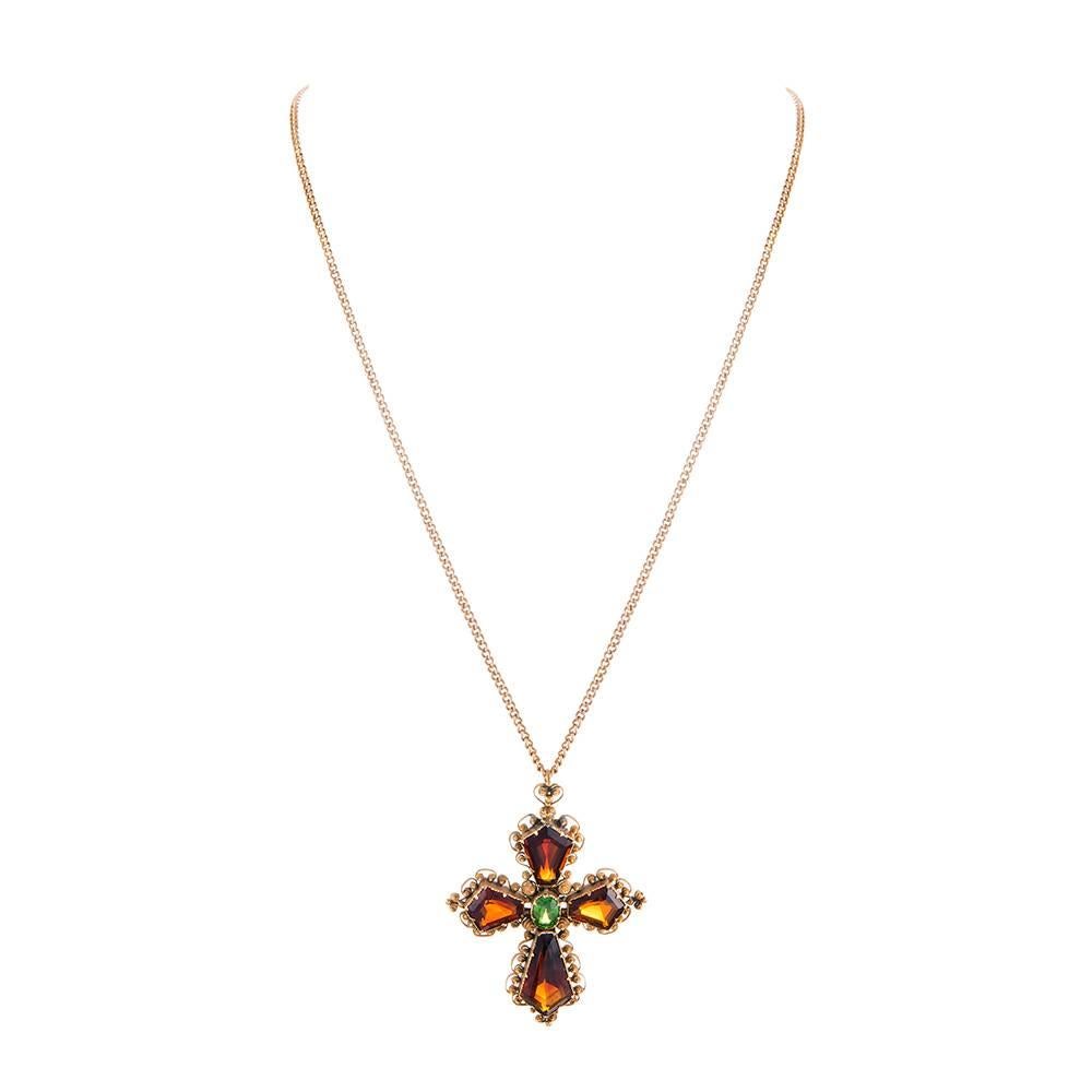 A lovely antique cross, decorated with richly hued garnets and bordered by a scrolling frame of gold. Note the bale. The cross measure 2 by 1.5 inches and is offered on a 16 inch antique chain. Rendered in 15k yellow gold. 