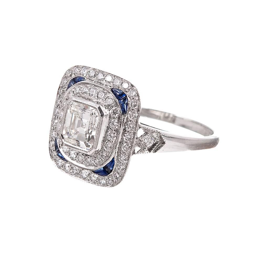 A platinum ring made in the art deco style and set in the center with a .51 carat asscher cut diamond, then framed with two rows of round brilliant diamonds and finished with sapphire accents at the corners. The center diamond grades as I-J color