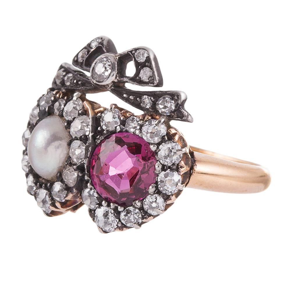Silver over 18k yellow gold ring with two hearts, side-by-side, set in the center with a pearl and a one carat dark pink ruby. Each heart and the bow that sits atop them, is framed by old European cut diamonds. This motif is a popular theme in