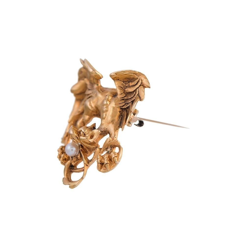 18k yellow gold griffin grasping a solitary pearl in his mouth, a lovely large example measuring 2 by 1.5 inches, created with incredible detail. Note the texture of the feathers on his wings and taloned feet. The piece is finished with a pin back
