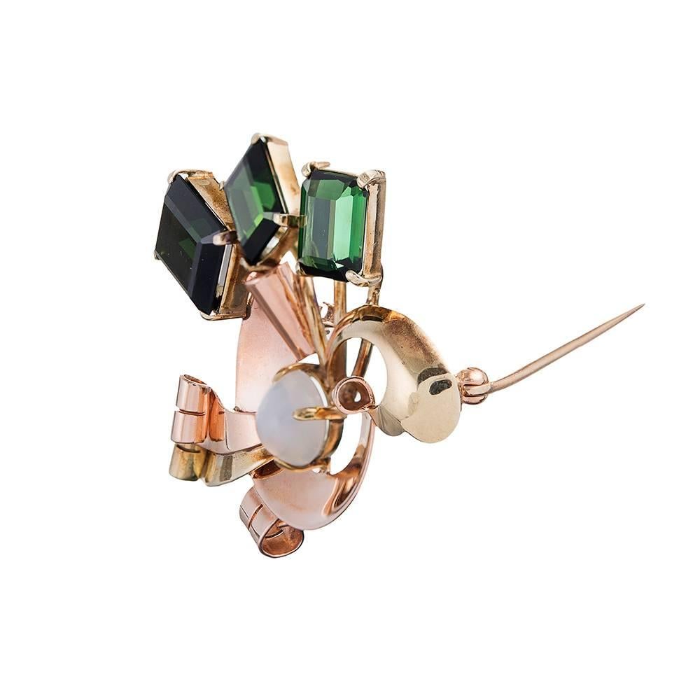 A marvelous rendering of classic retro style, created in 14 karat yellow and rose gold. Set with a trio pf emerald cut green tourmalines and anchored in the center with a moonstone cabochon, the scrolling retro design is a fun and sophisticated bit